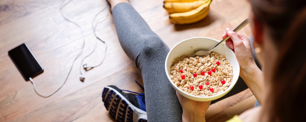 Woman in workout clothes eating oatmeal with berries