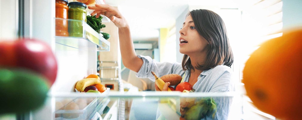 Woman picking out fruit and veggies from fridge