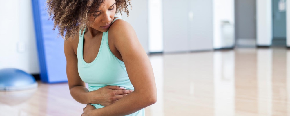 Woman grabbing stomach experiencing digestive pain while working out