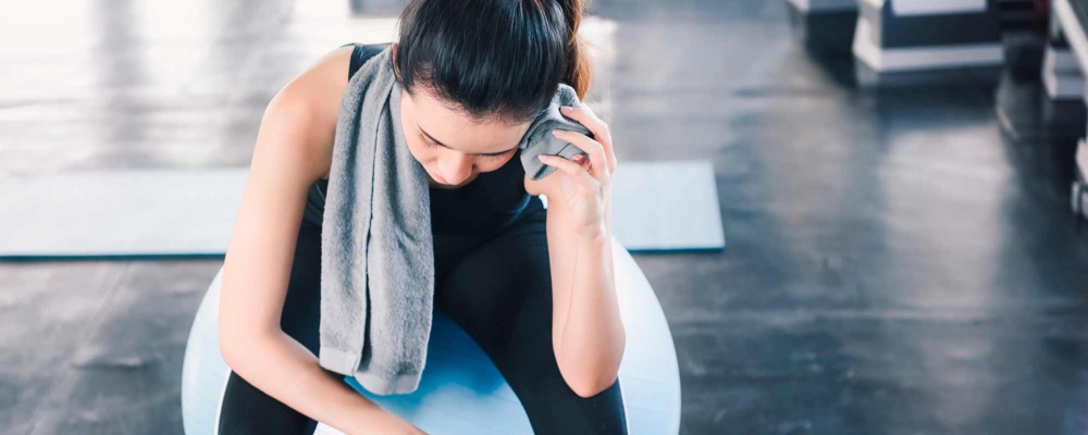 Woman sitting on exercise ball wiping sweat off forehead post-workout