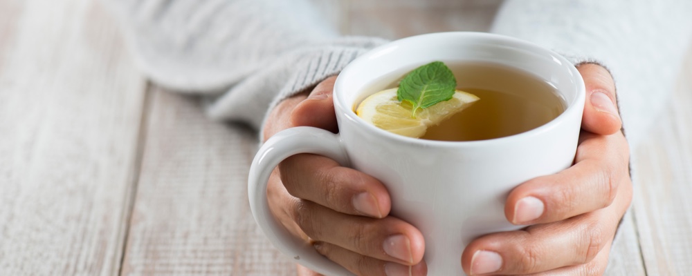 Person holding warm cup of tea to sooth flu symptoms 