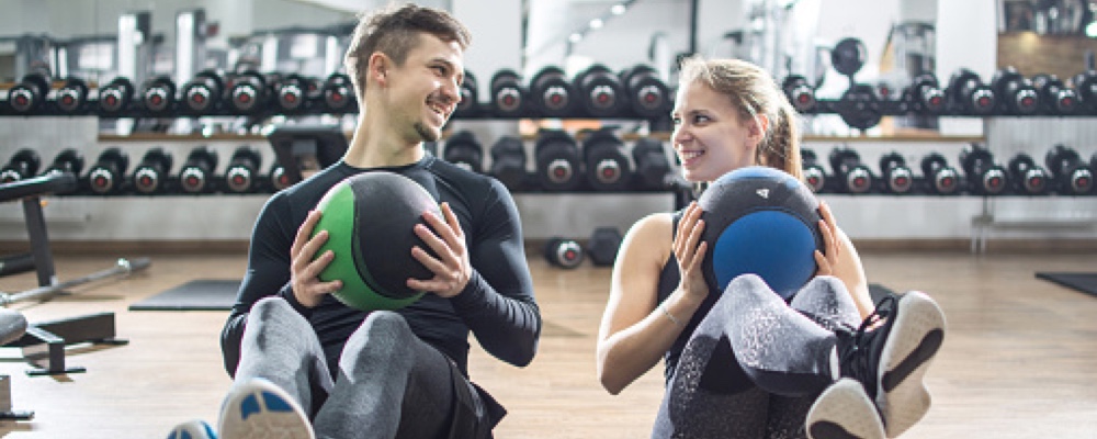 Fit couple doing abdominal exercise with fitness balls at club