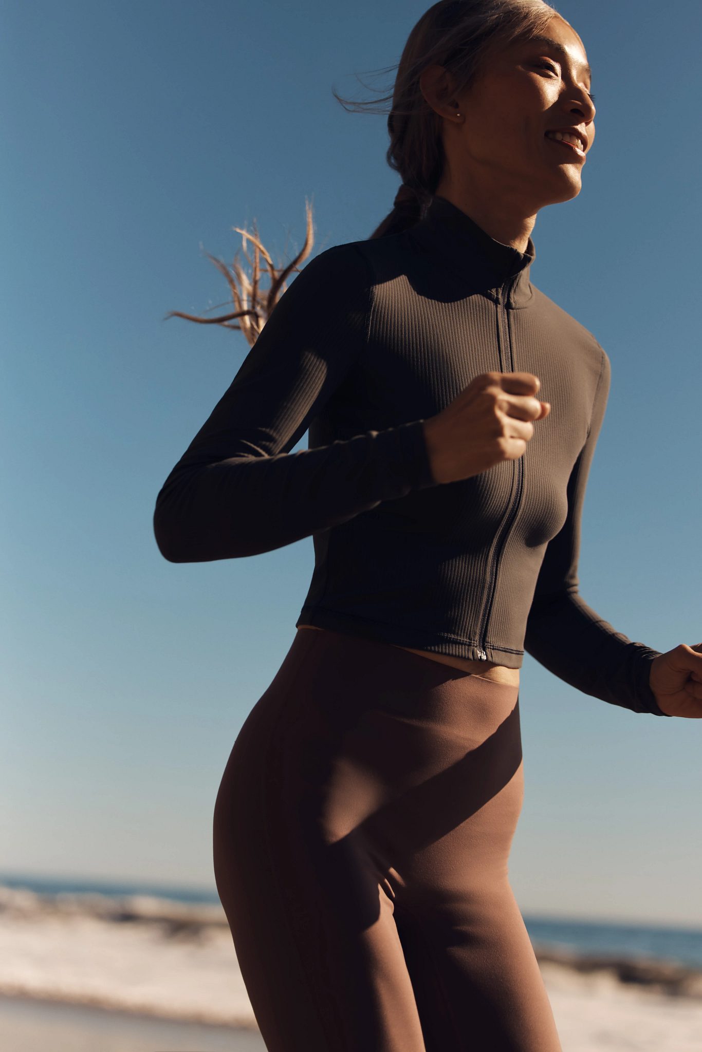 An adult woman running on the beach with the ocean in the bacground