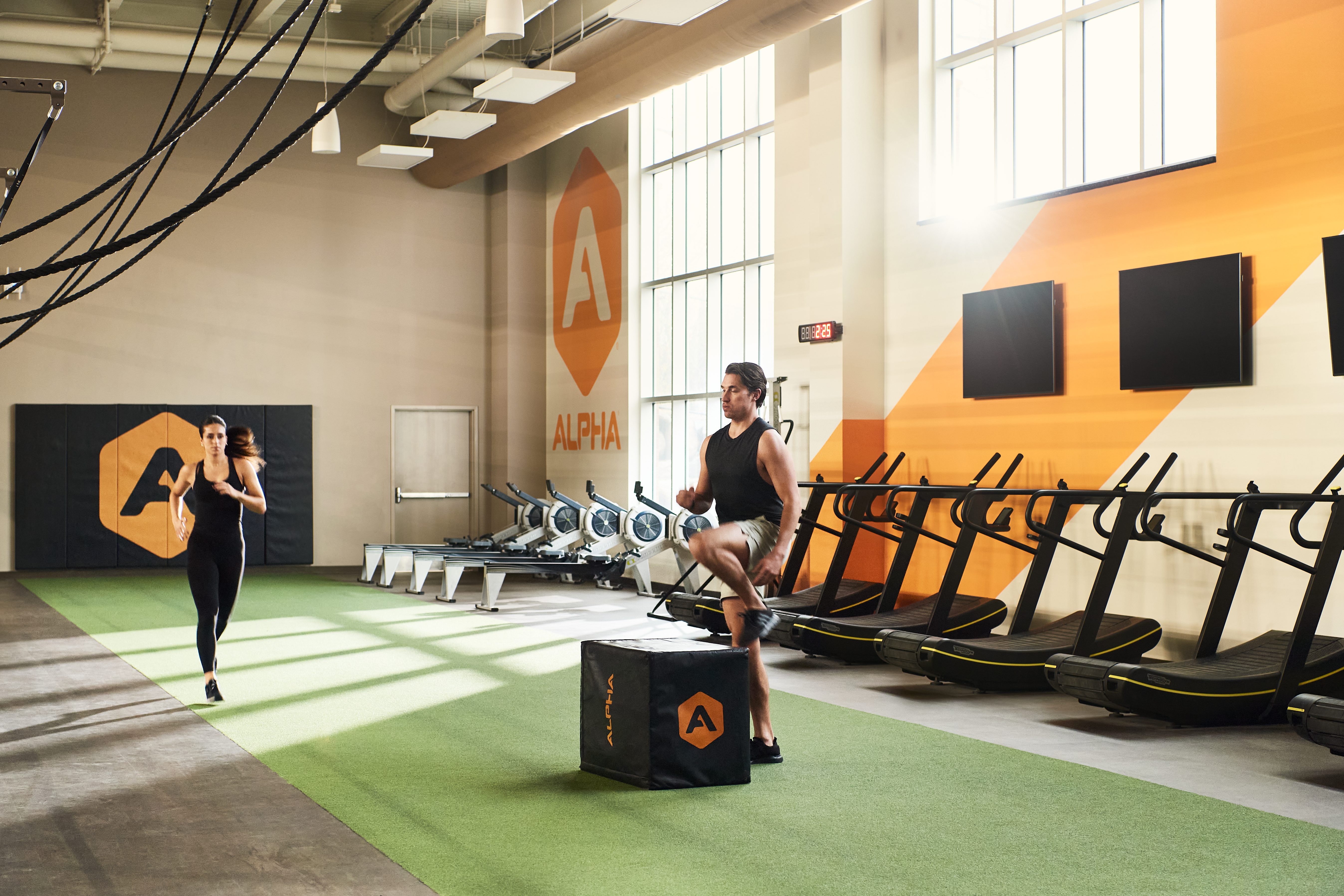 A male doing box jumps and a female jogging in an Alpha Studio