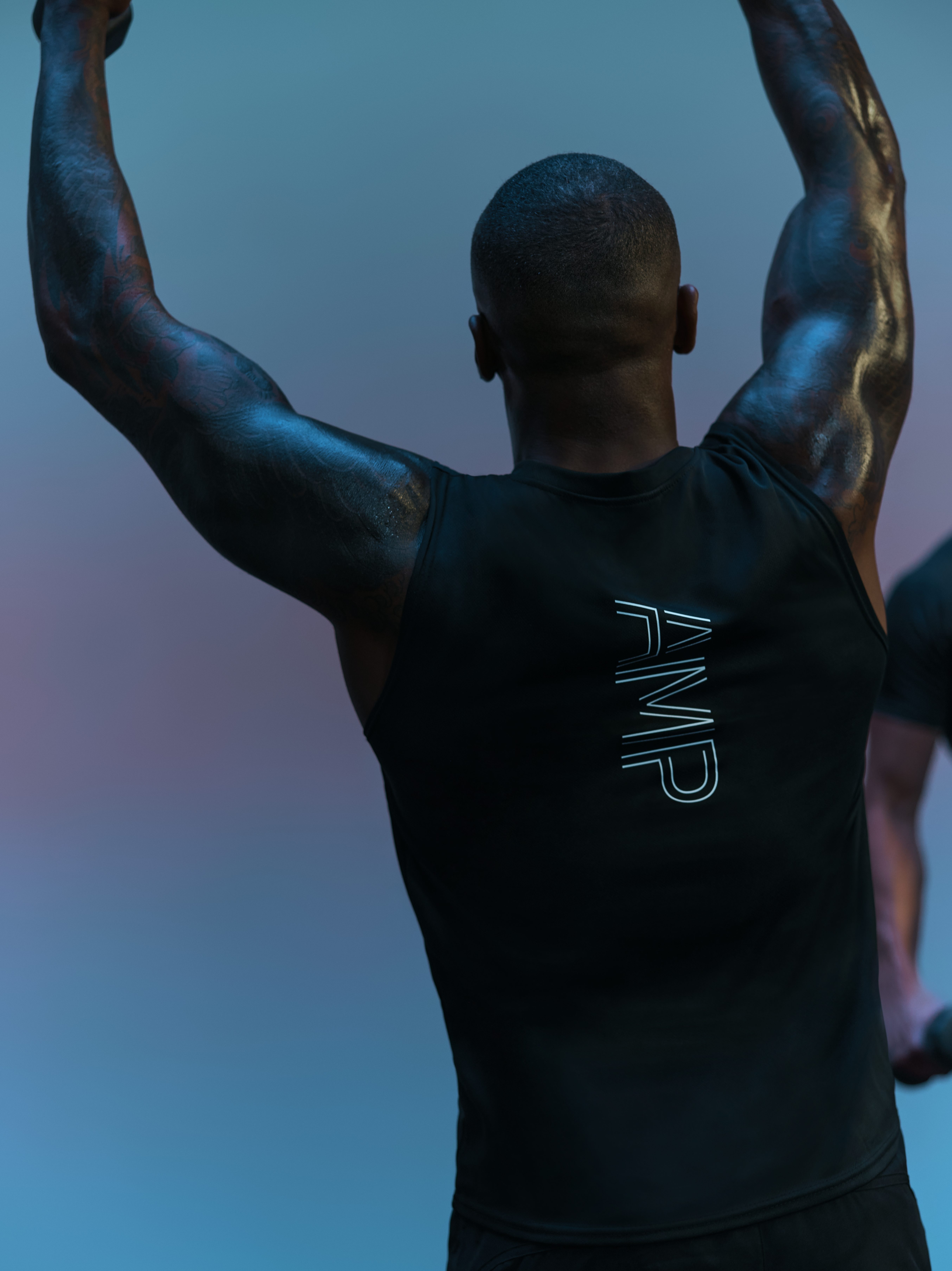 The back of a cyclist with their arms raised at an AMP spin class and AMP written on the back of their shirt