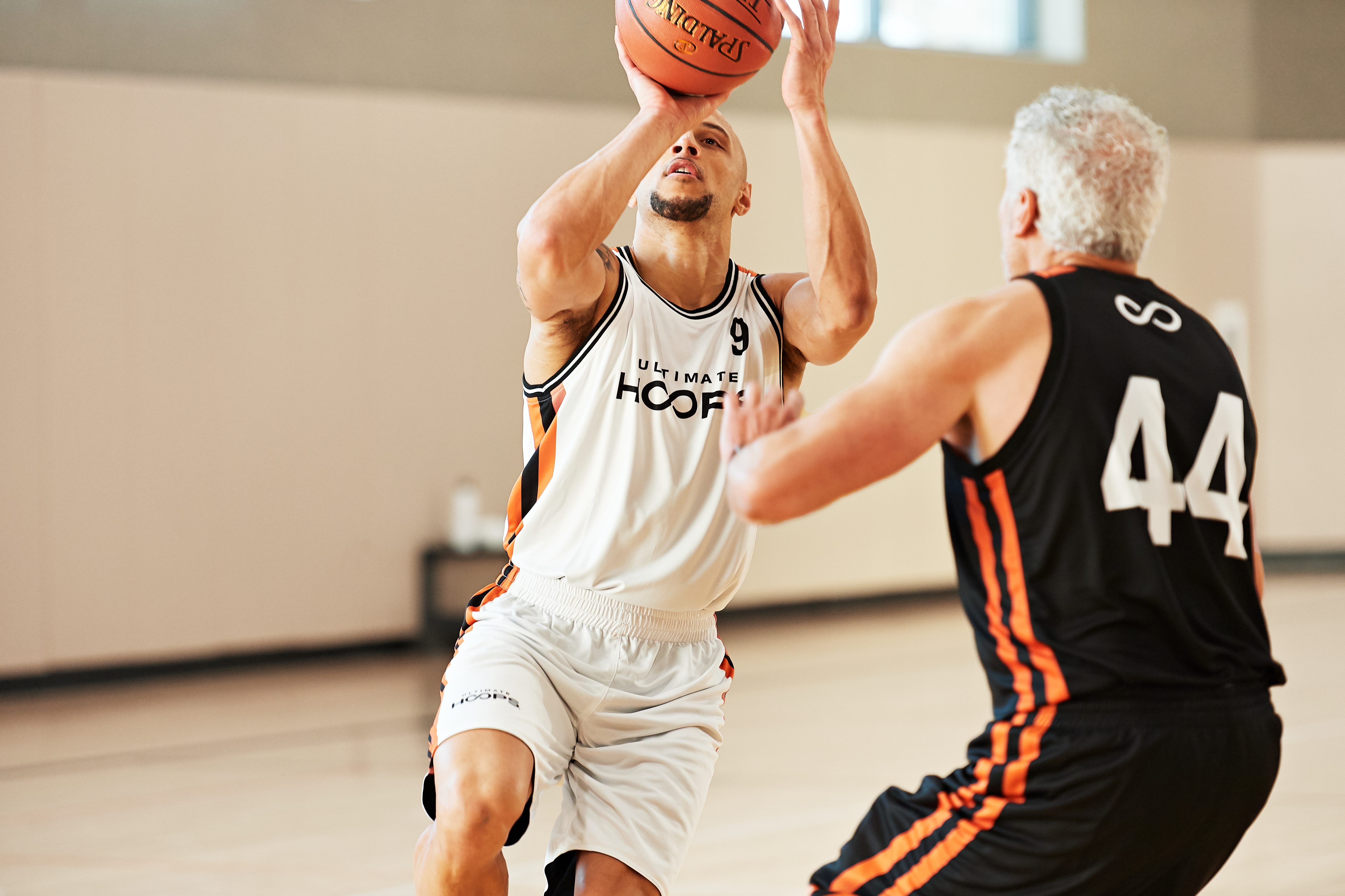 two males playing basketball - one making a shot, one blocking/defense