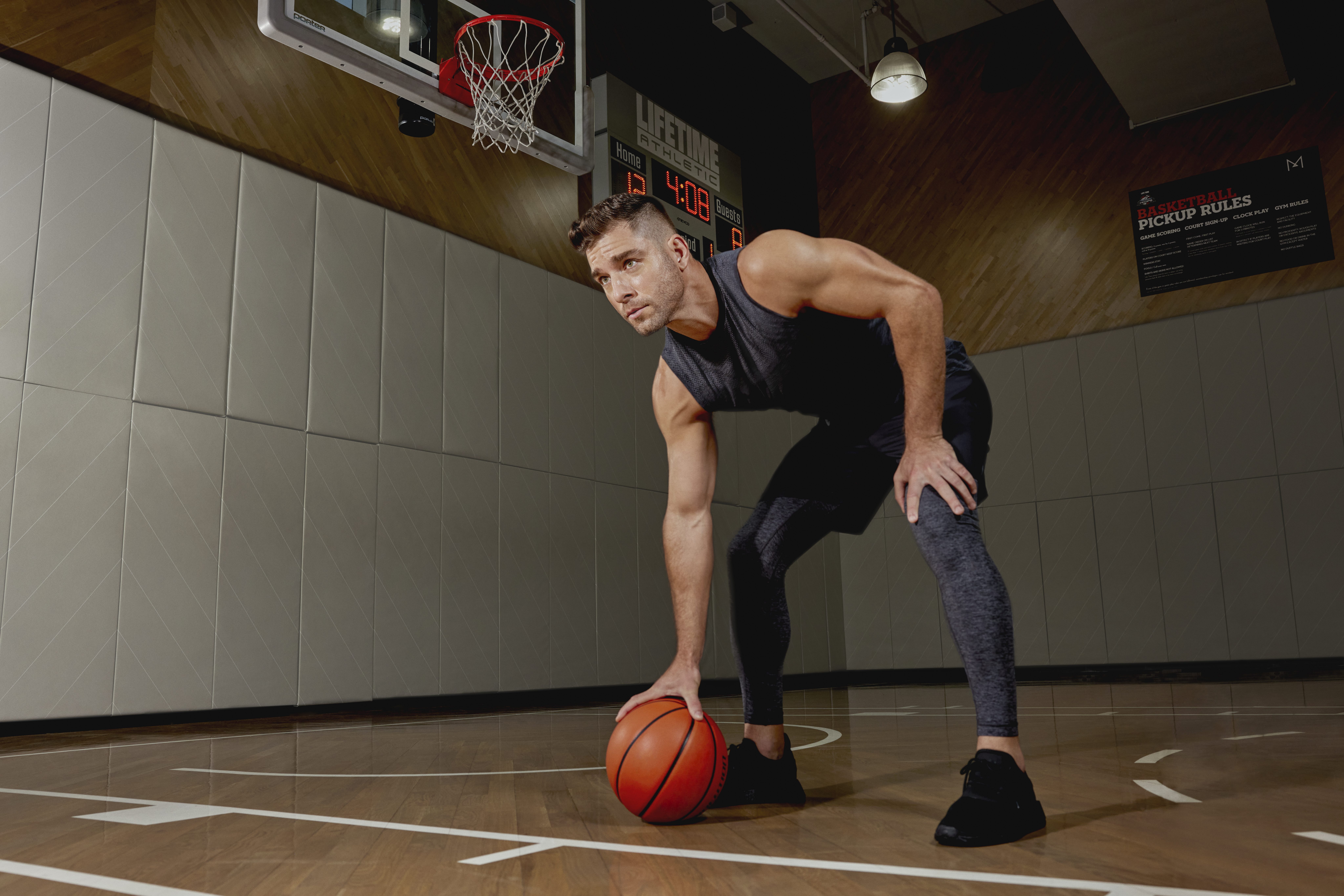 An adult man bent over holding a basketball on a wooden basketball court