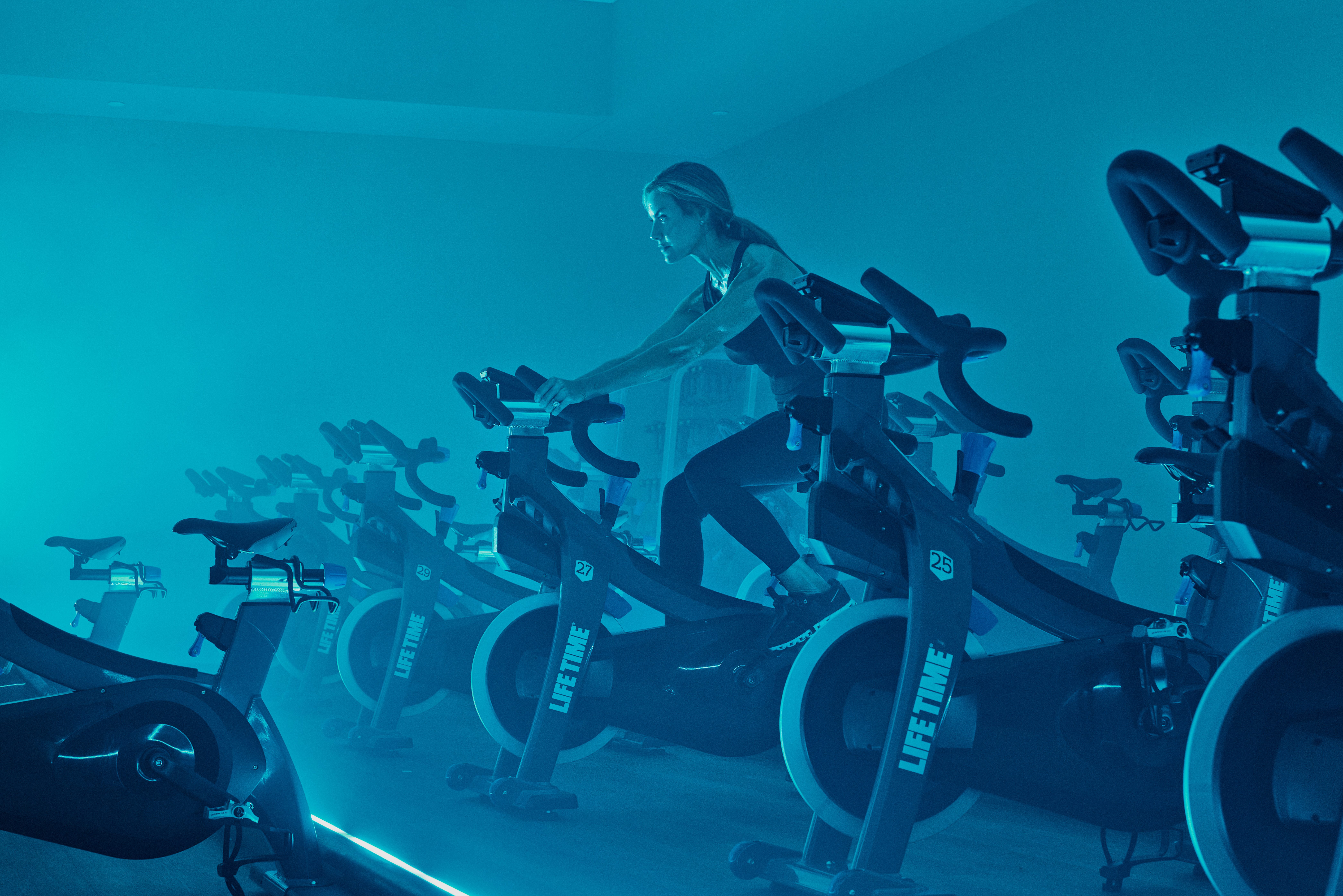 A female sitting on a stationary bike in a blue-lit cycle studio
