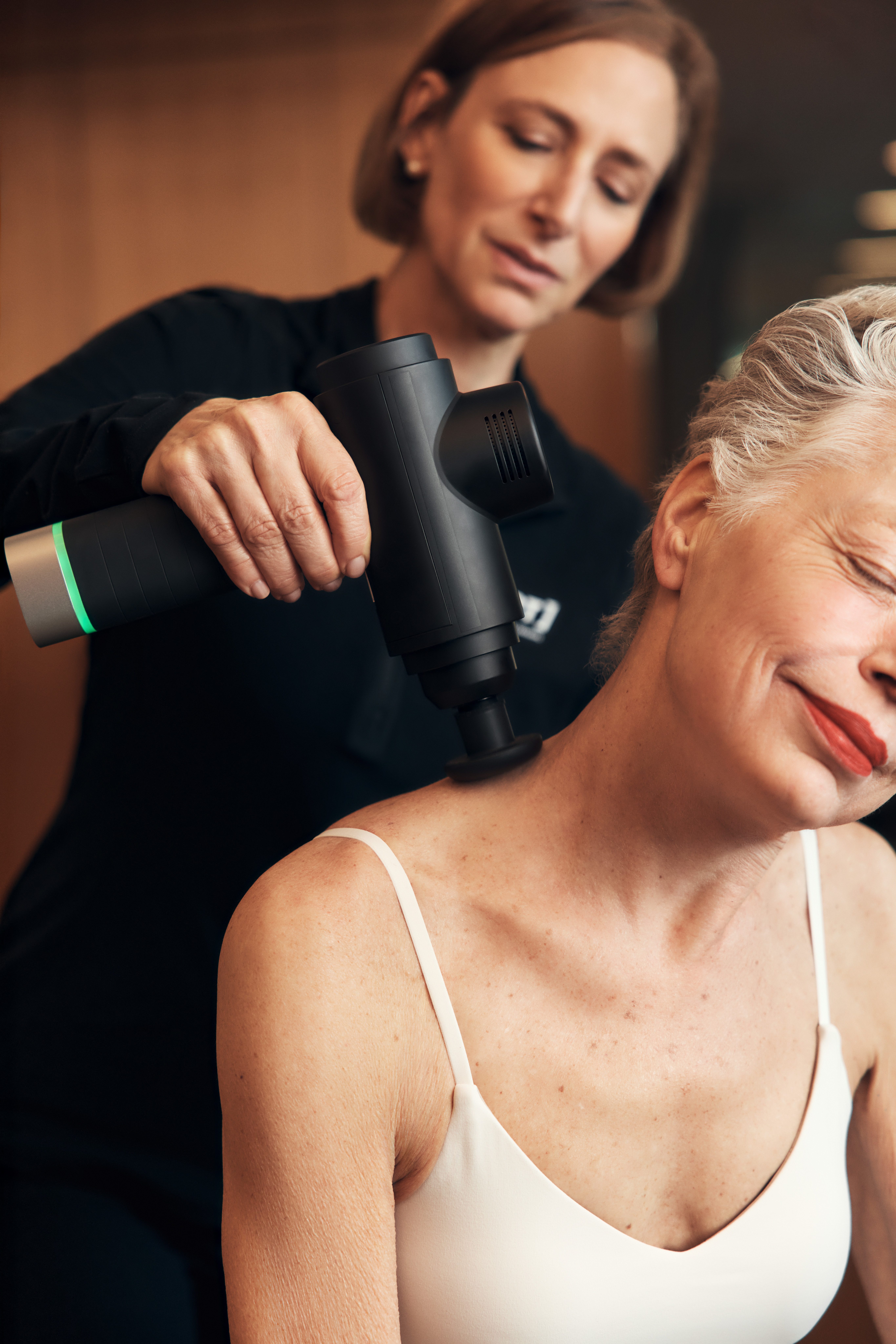 A Life Time Dynamic Personal Trainer massaging a client's neck with a massage gun