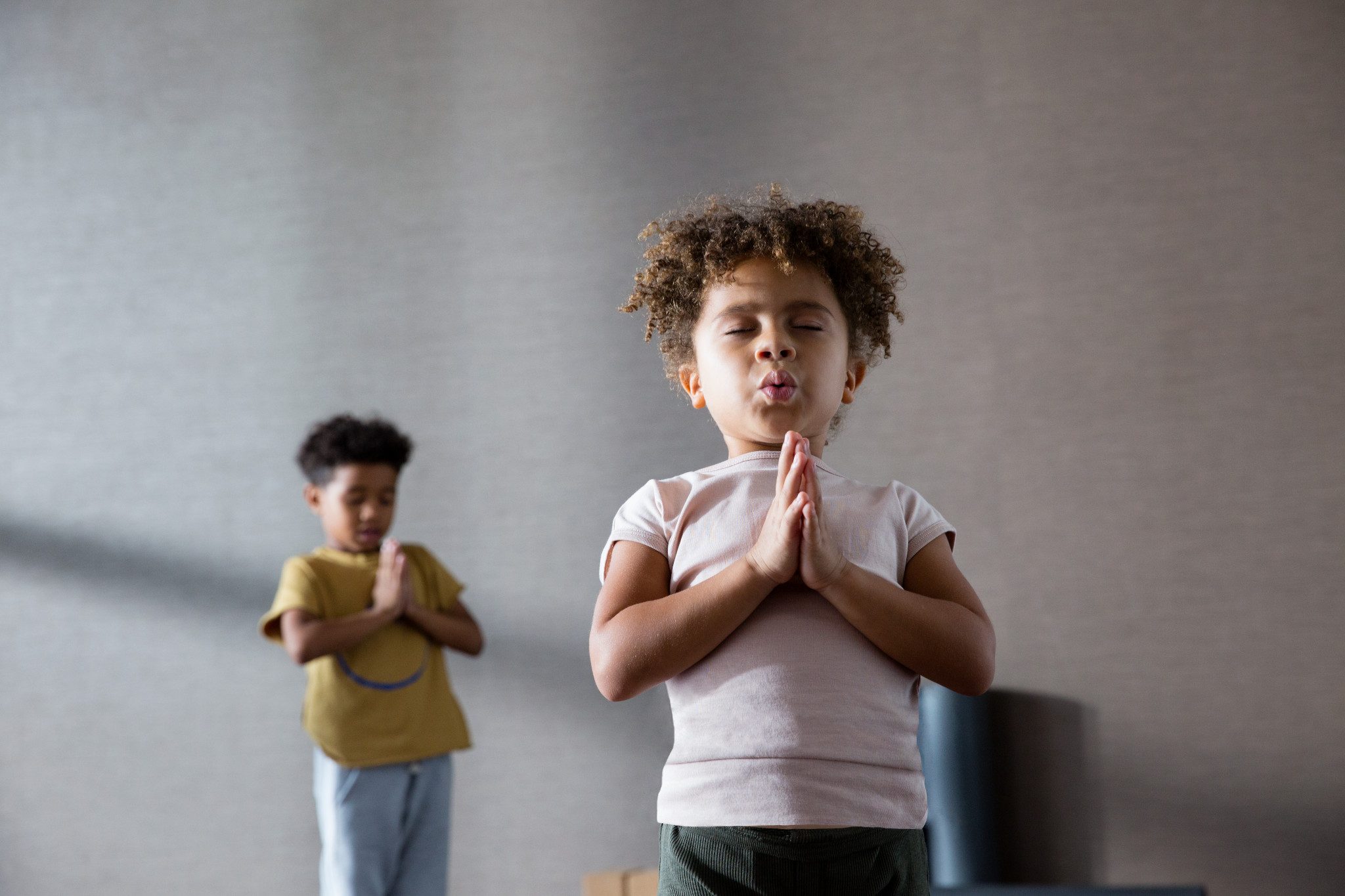 A young girl standing with hands in prayer pose with eyes closed during a kids yoga class at Life Time