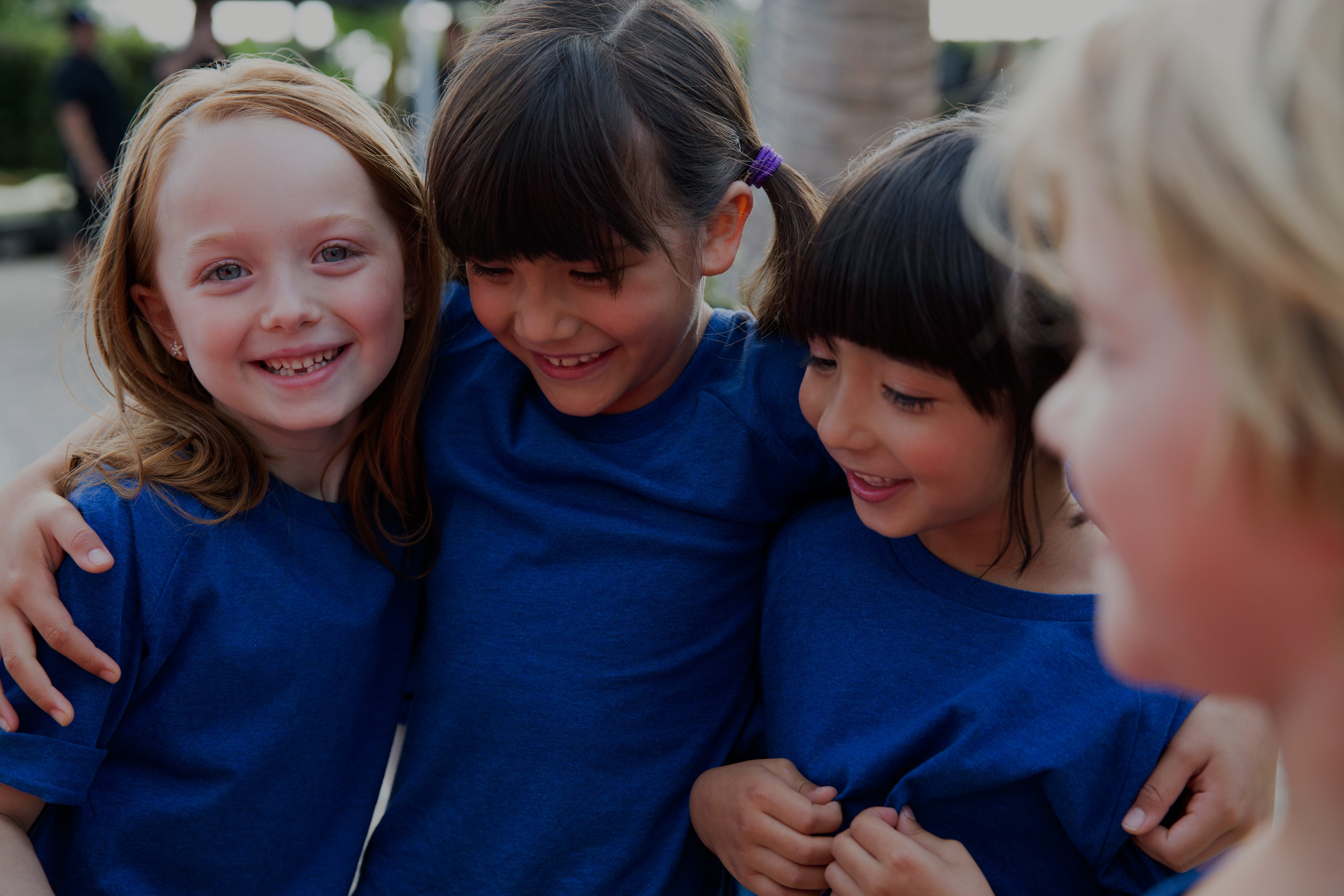Close view of three female children wearing blue T-shirts huddled together with their arms around each other
