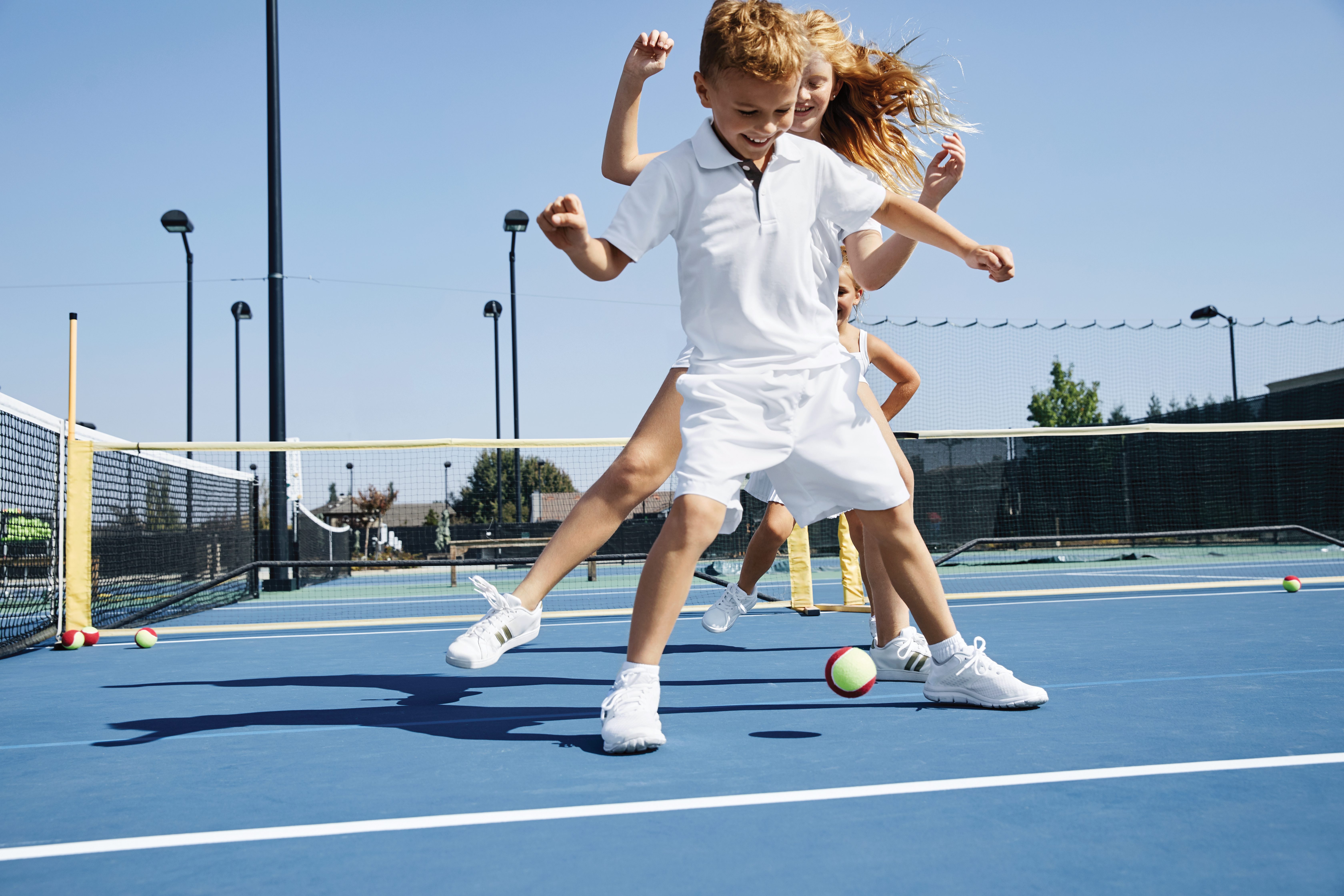 A group of children playing on an outdoor tennis court