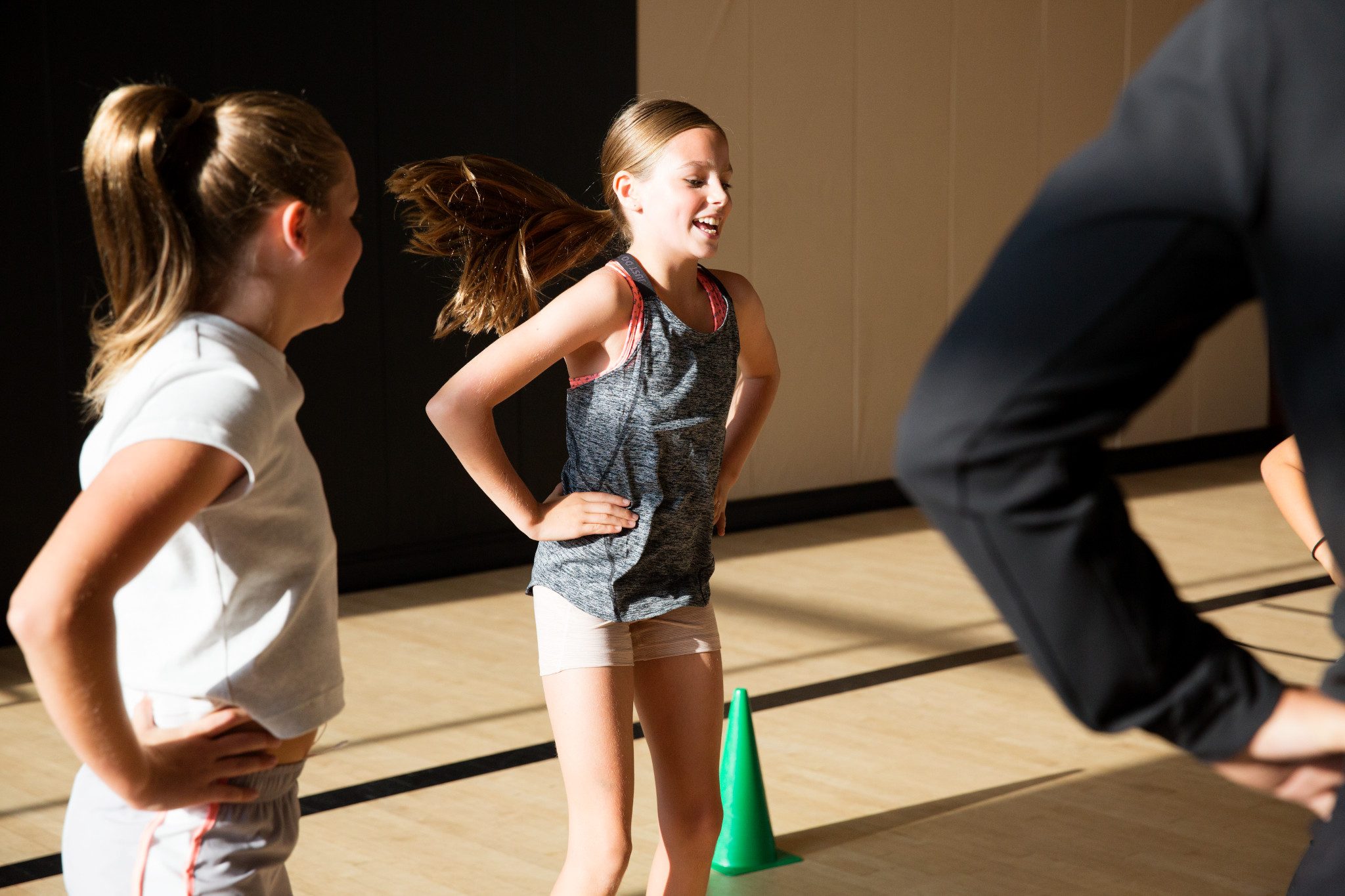 Two female children wearing athletic gear stand smiling with their hands on their hips in a Life Time gym