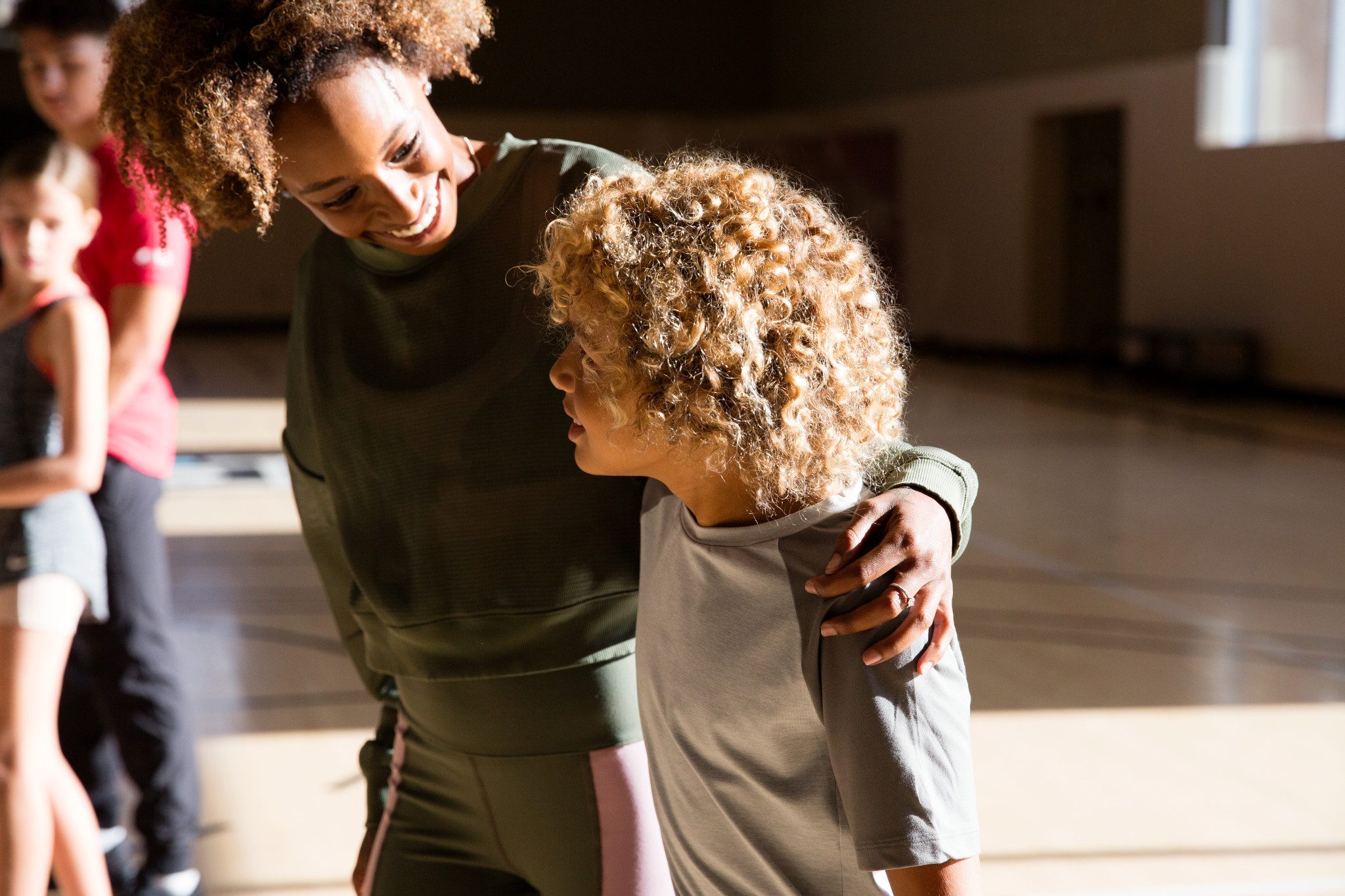 An adult female puts her arm around a male child in a gymnasium