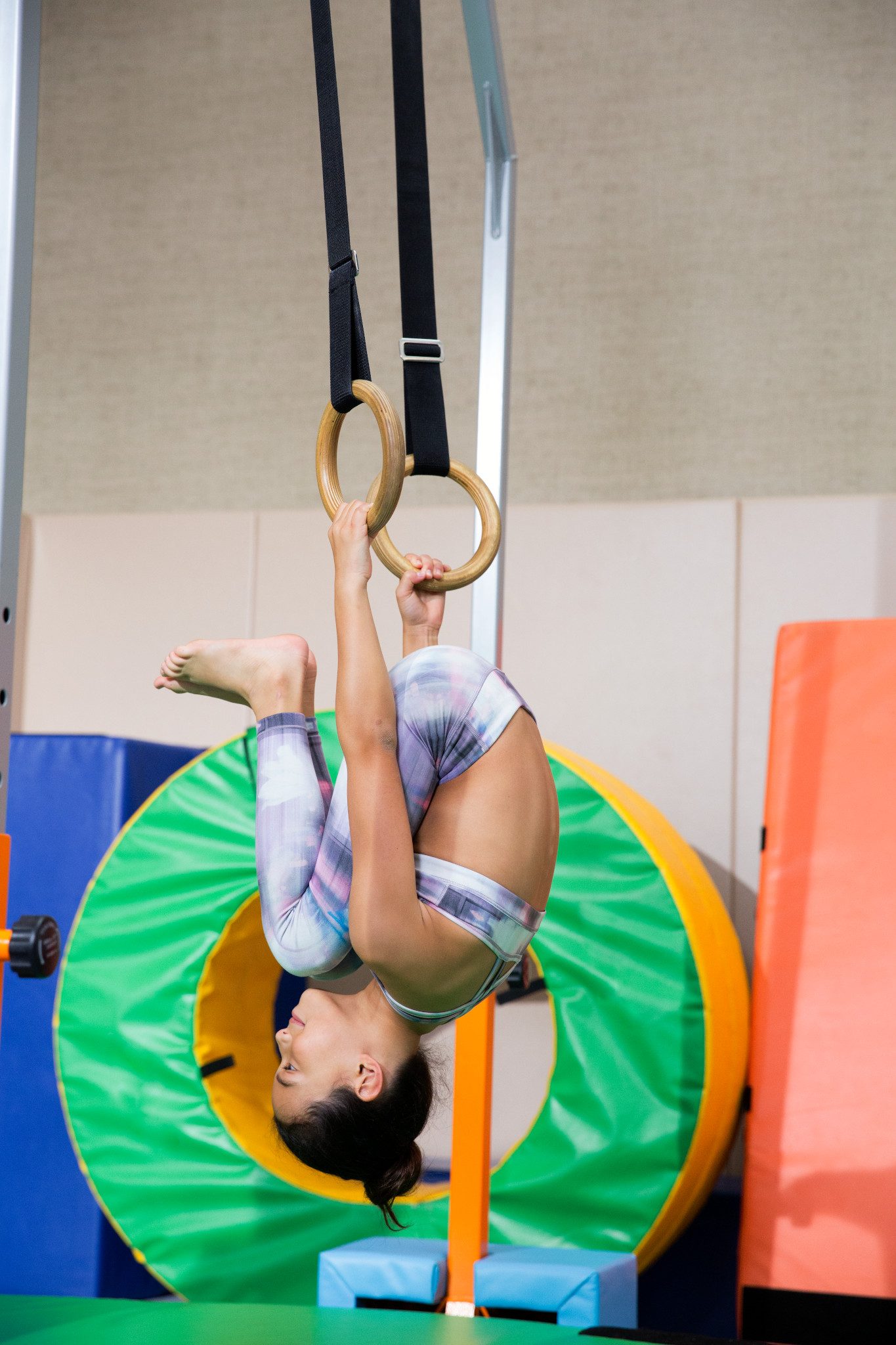 Young girl hanging upside down while holding onto gymnastics rings