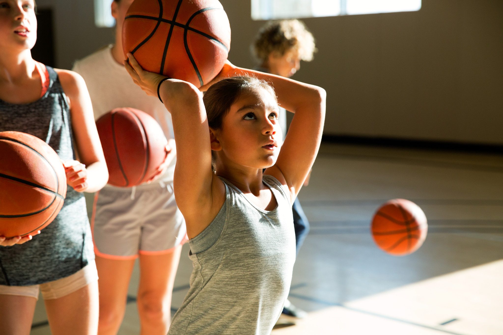 Close view of a female child holding a basketball above her head aiming at the basket