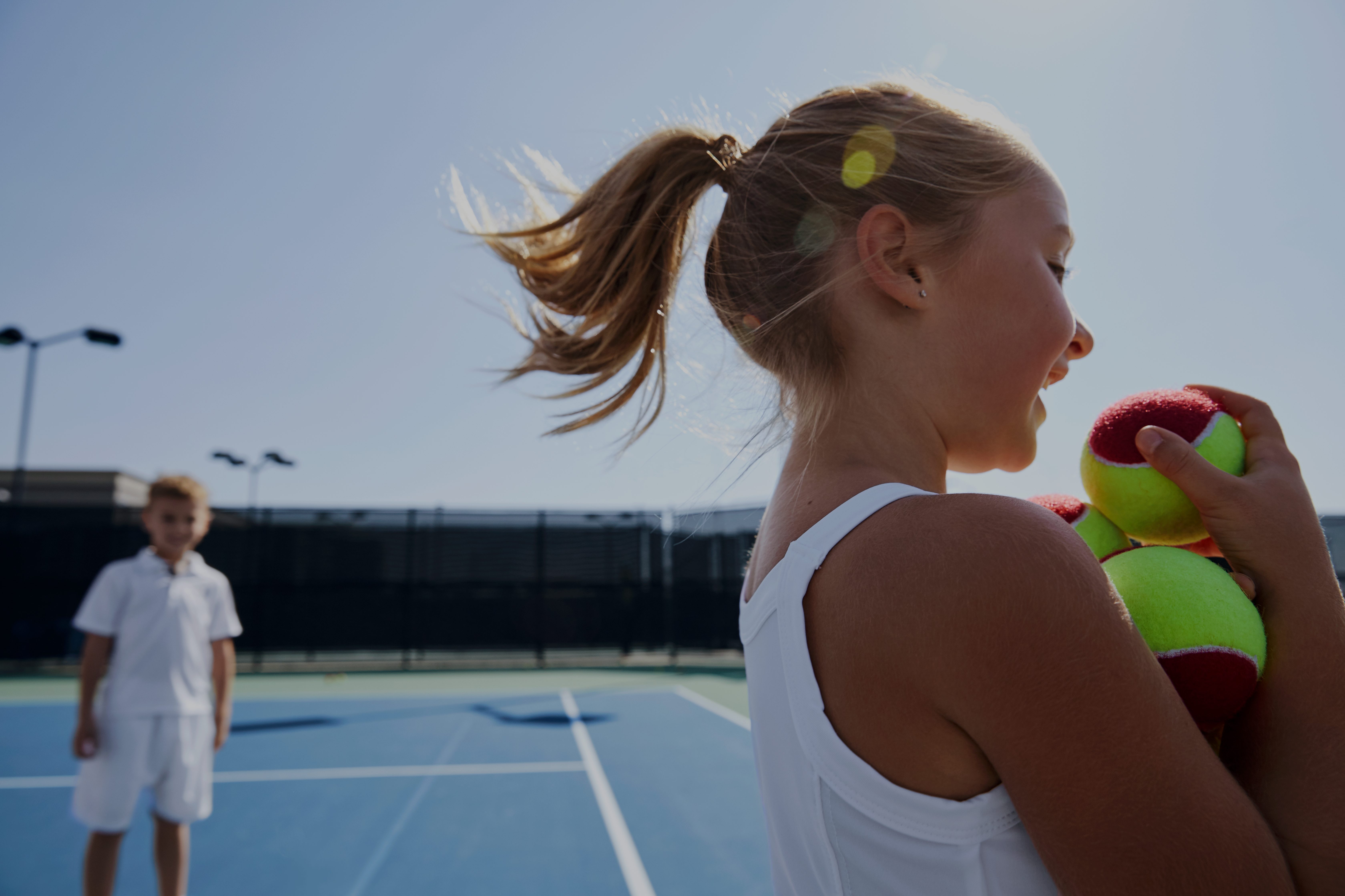 Close view of a female child holding tennis balls on an outdoor tennis court