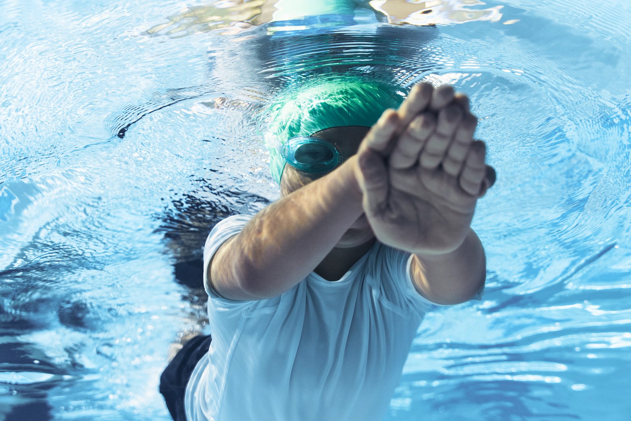 a boy in a green swim cap swimming under water