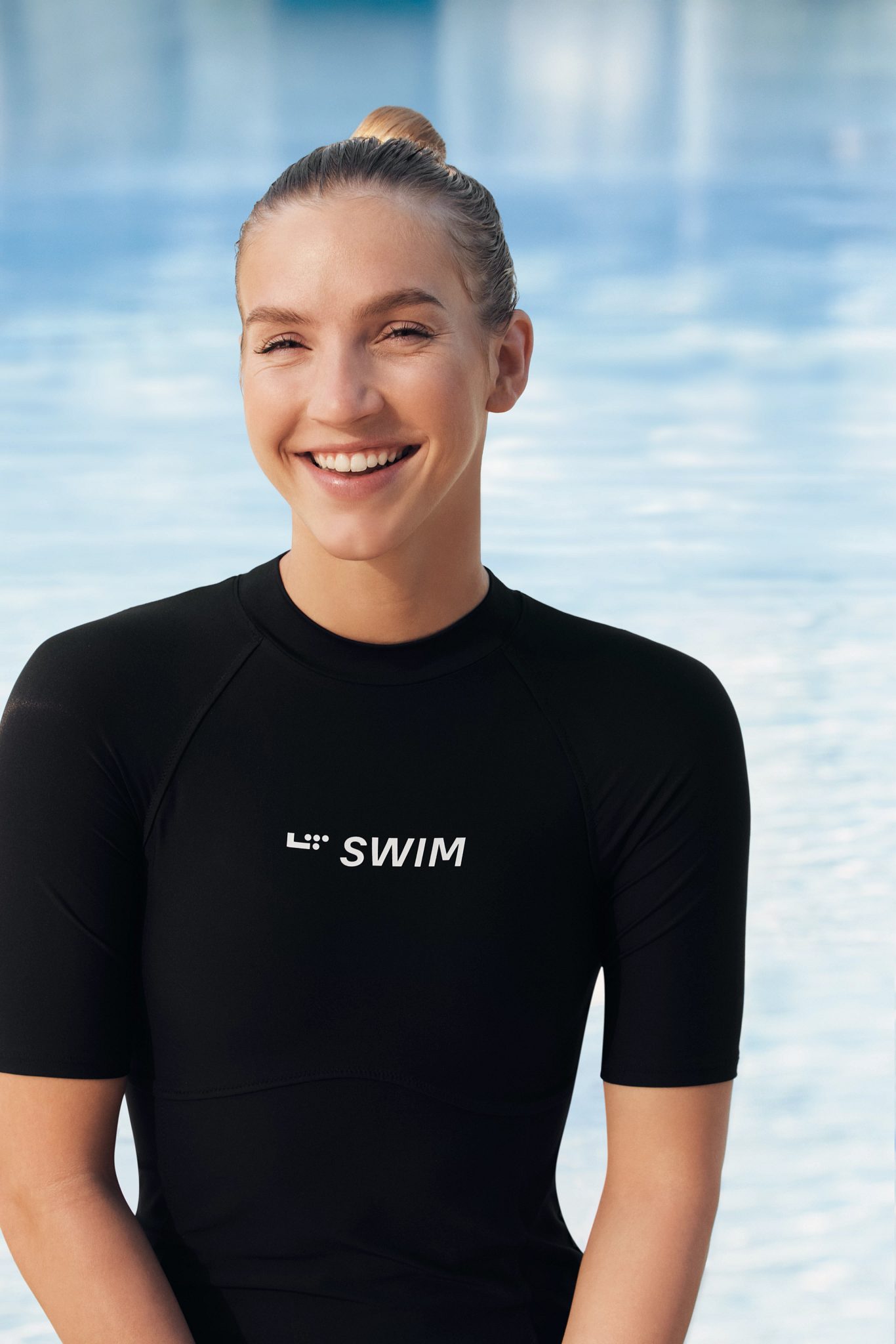 girl in a black L T swim shirt smiling by a pool