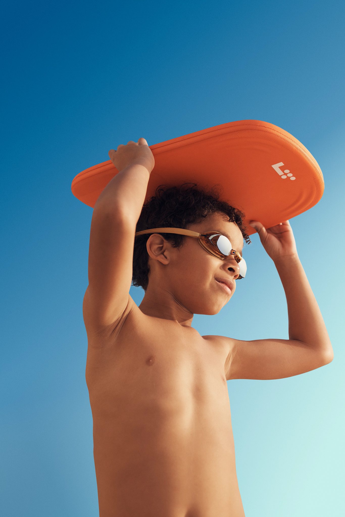 boy wearing swim goggles holding an orange kick board