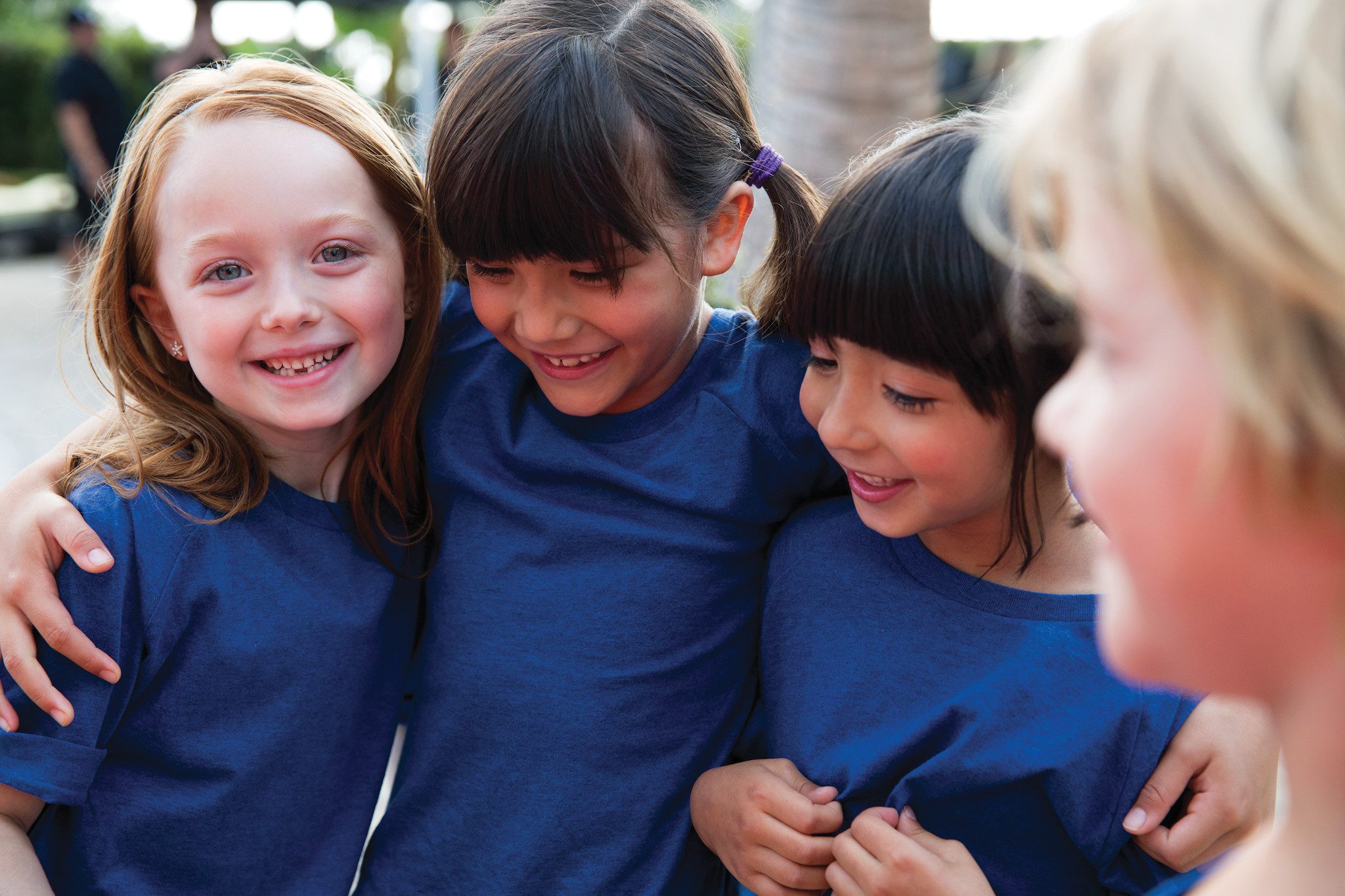 Close view of three female children wearing blue T-shirts huddled together with their arms around each other