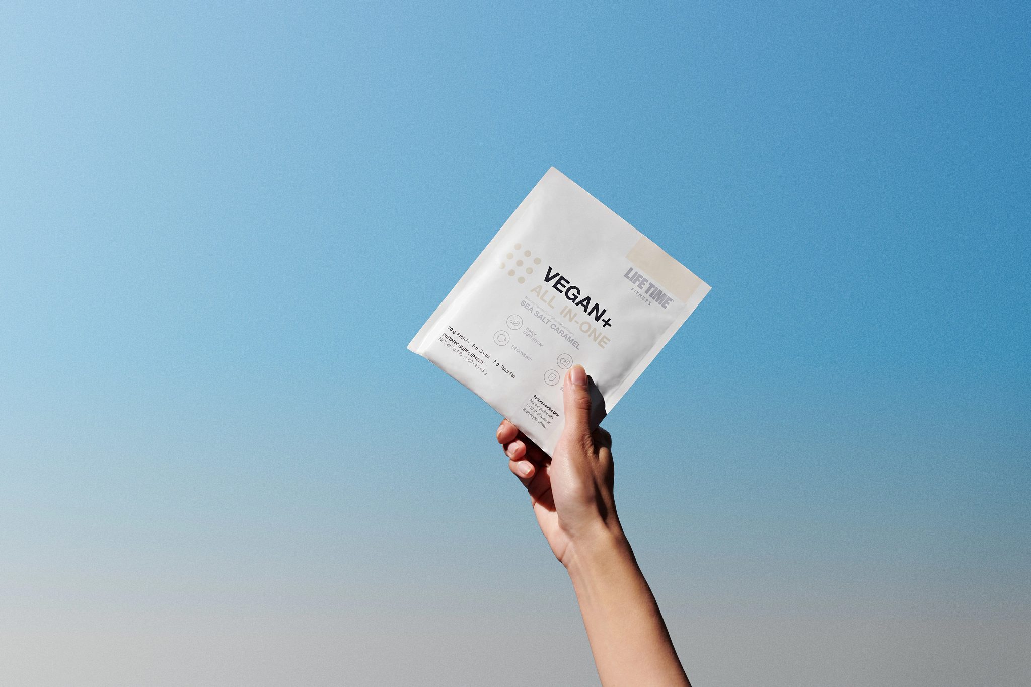 A female hand holding a packet of Sea Salt flavored Vegan+ All In-One in the air