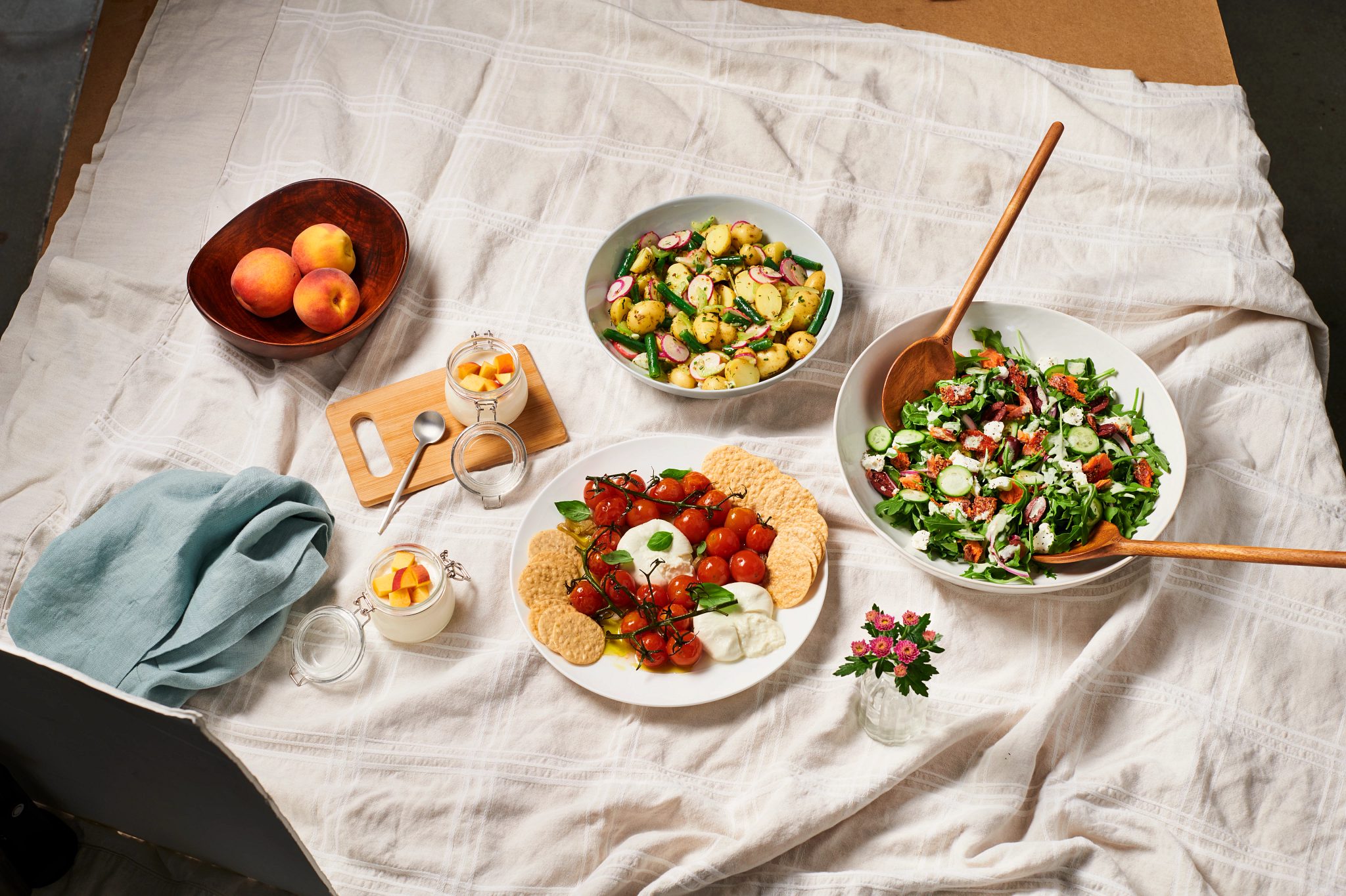 An indoor picnic set up with two veggies salads, one with salmon and peaches and cream sitting on a cream table cloth.