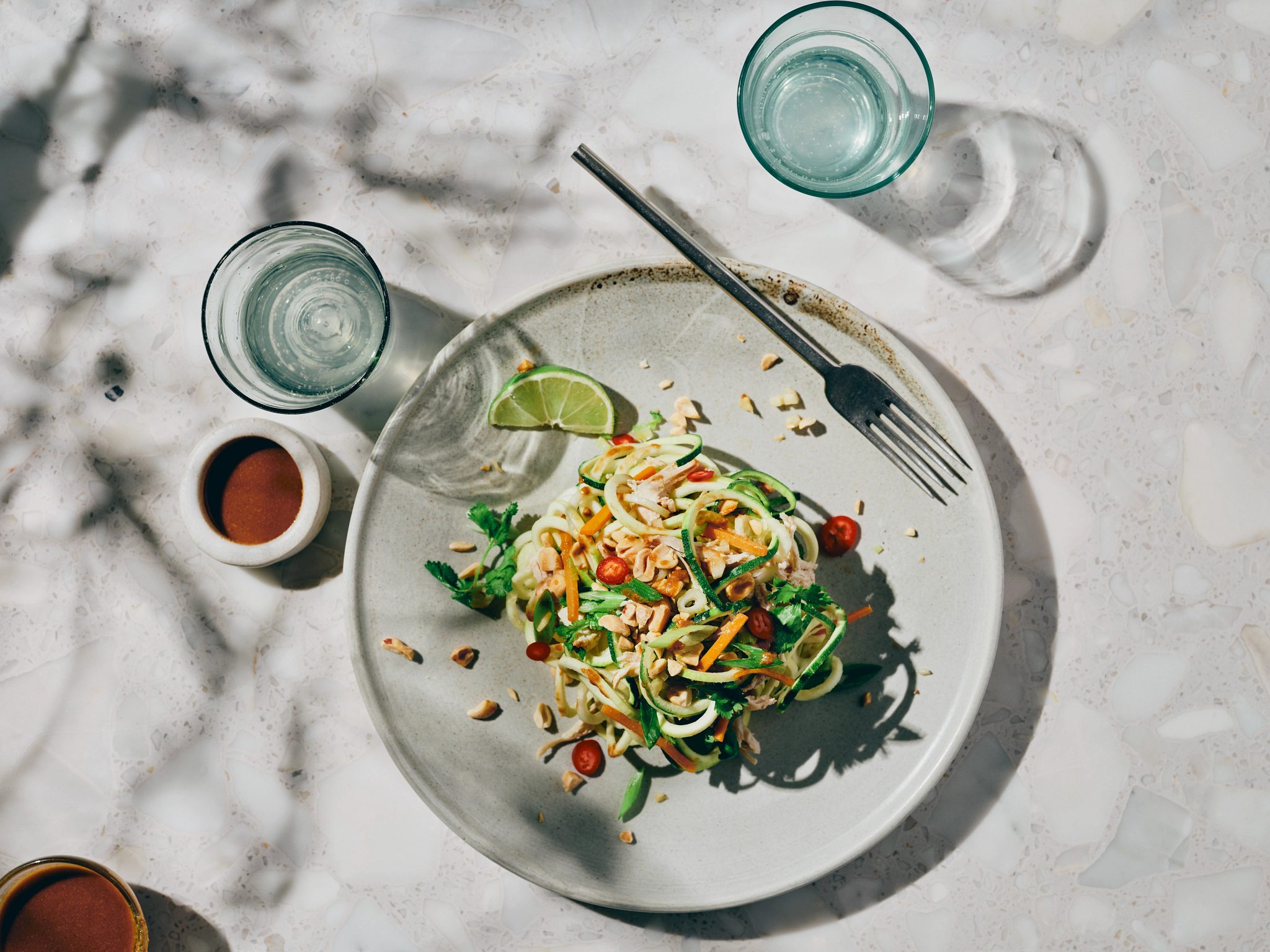 Overhead view of a plate topped with zucchini noodles and a lime slice