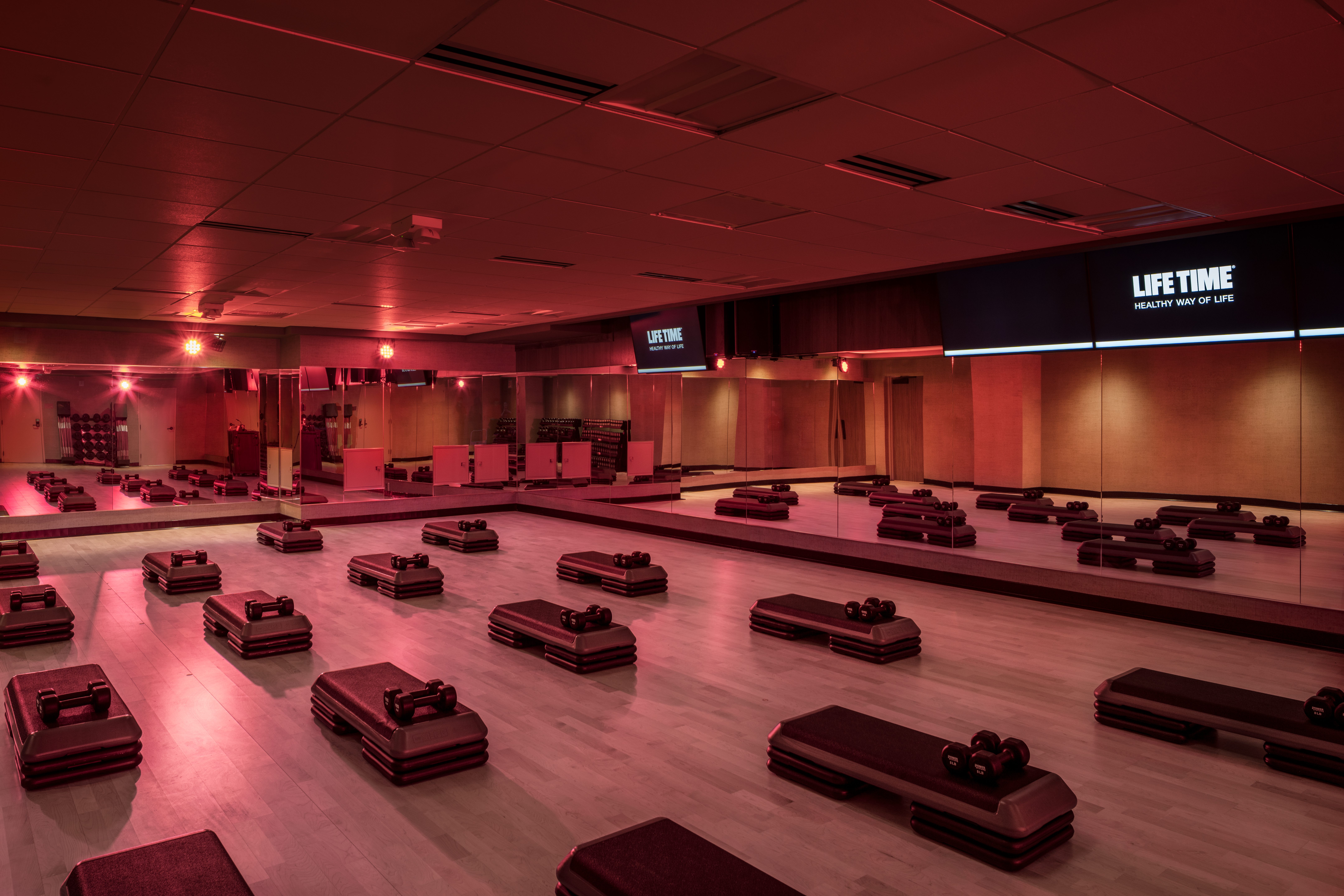 a Life Time Group Fitness Studio with mirrors, aerobic step blocks, and dumbbells