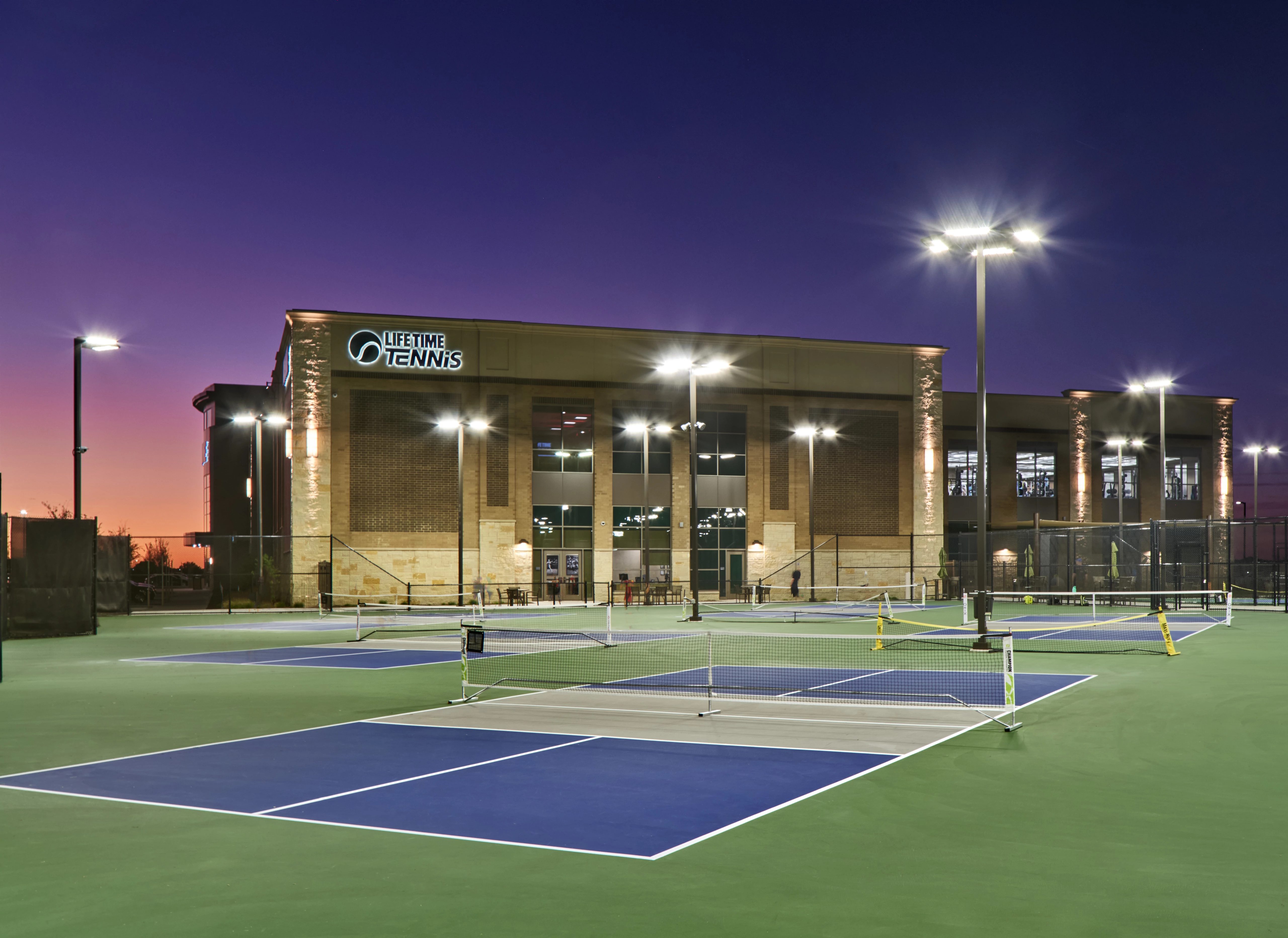 3 outdoor pickleball courts outside a Life Time at dusk