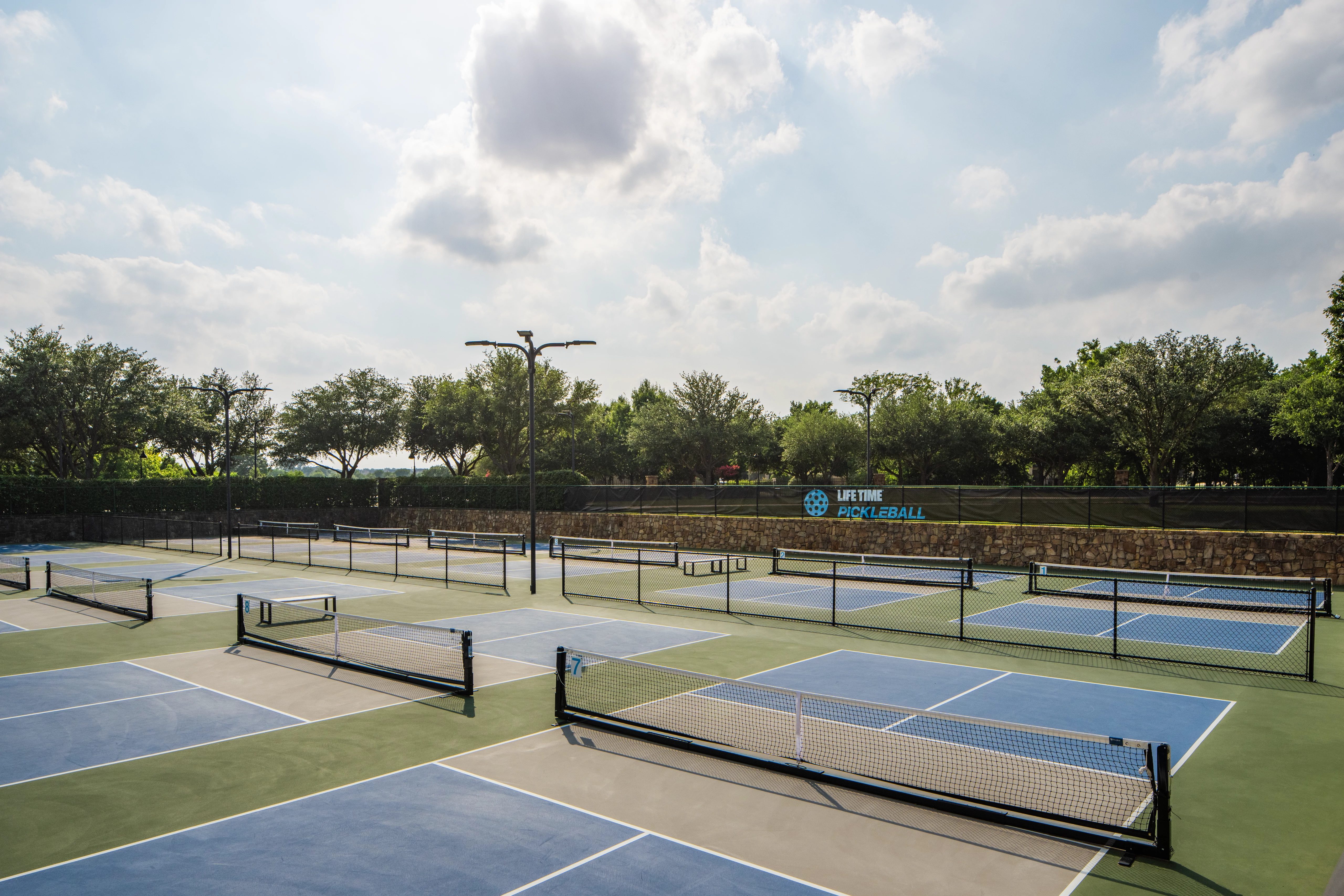 12 outdoor pickleball courts, surrounded by a stone wall and lush trees