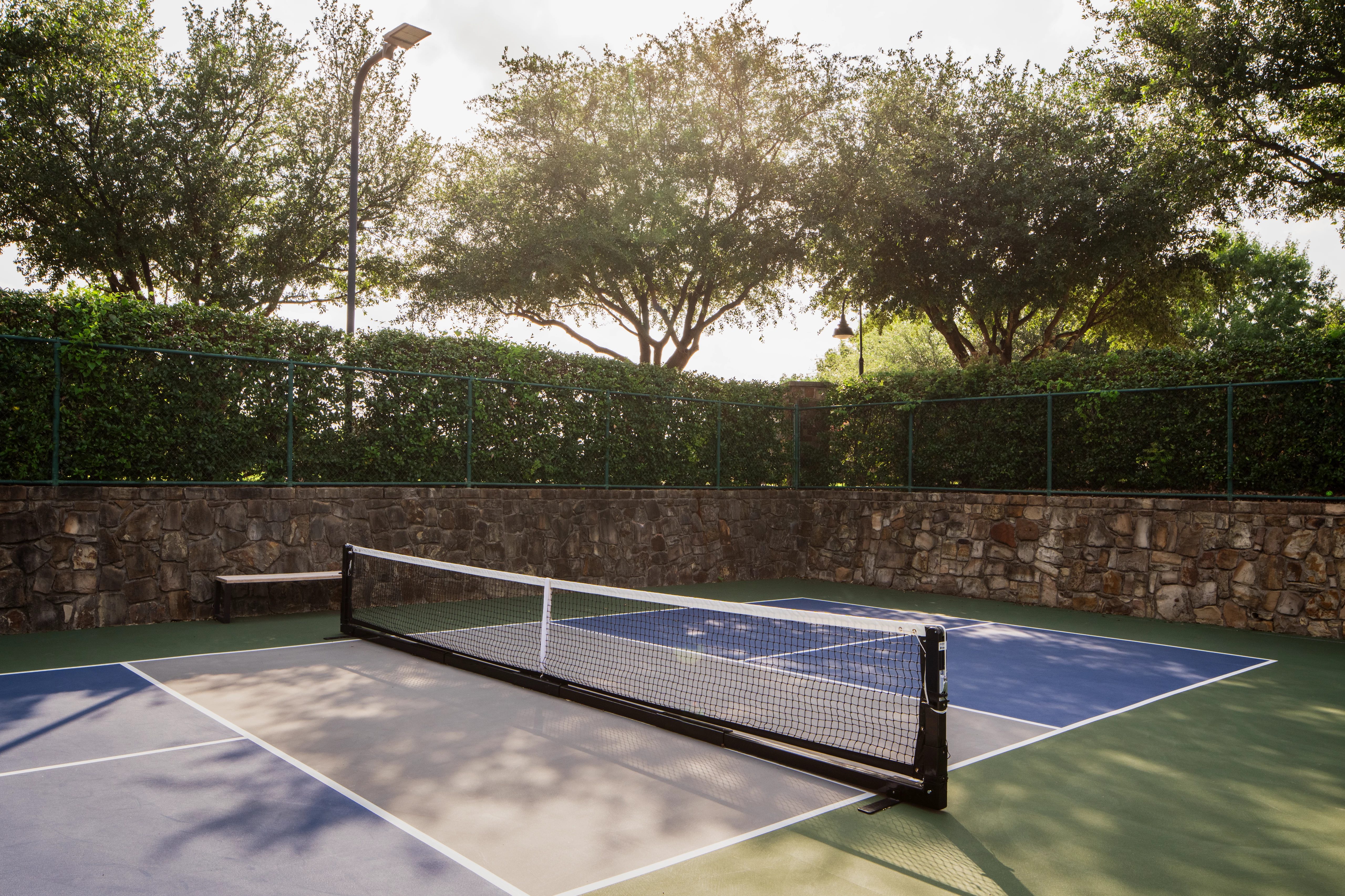 An outdoor pickleball court surrounded by a stone wall and tall trees