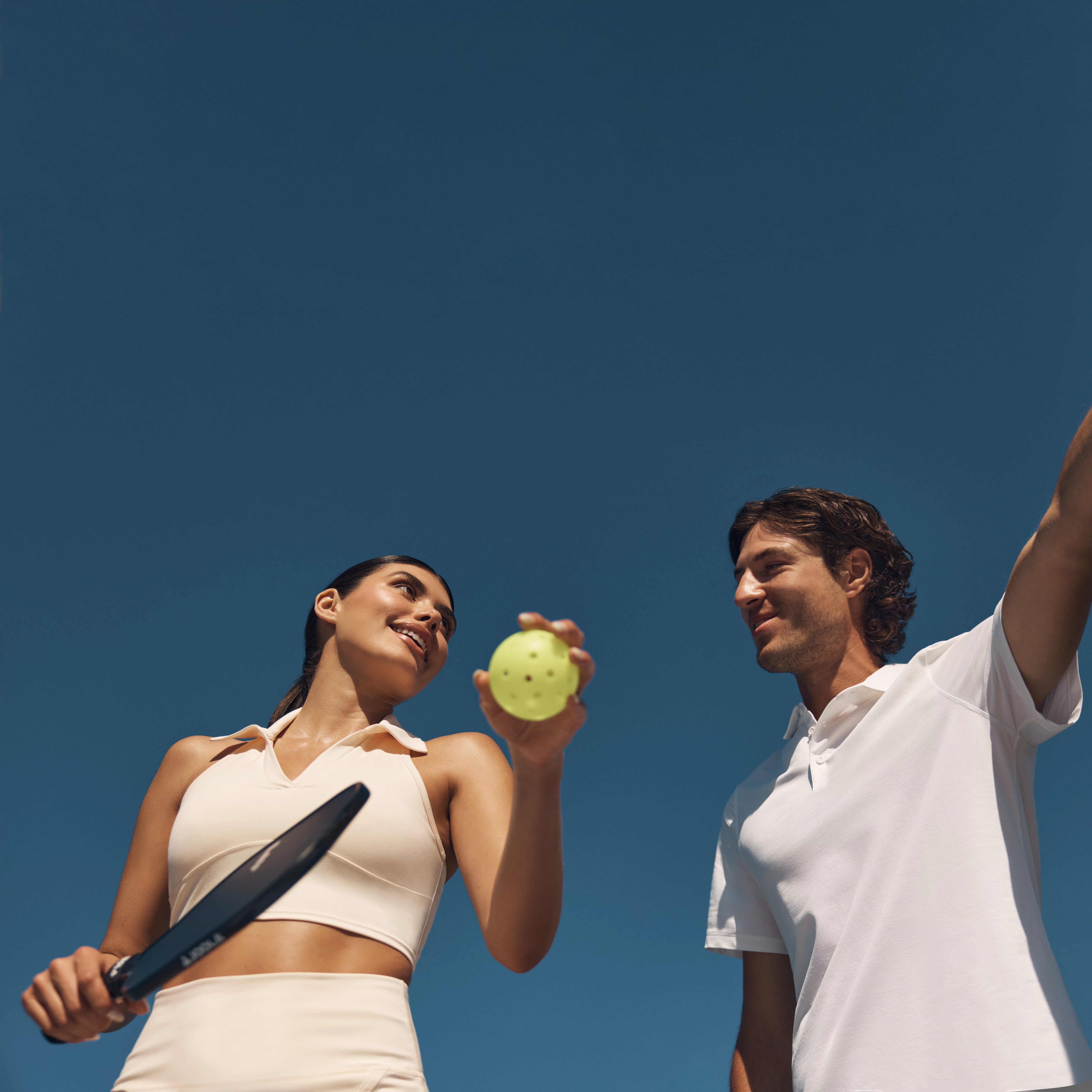 Two pickleball players looking at each other while holding a ball and paddle