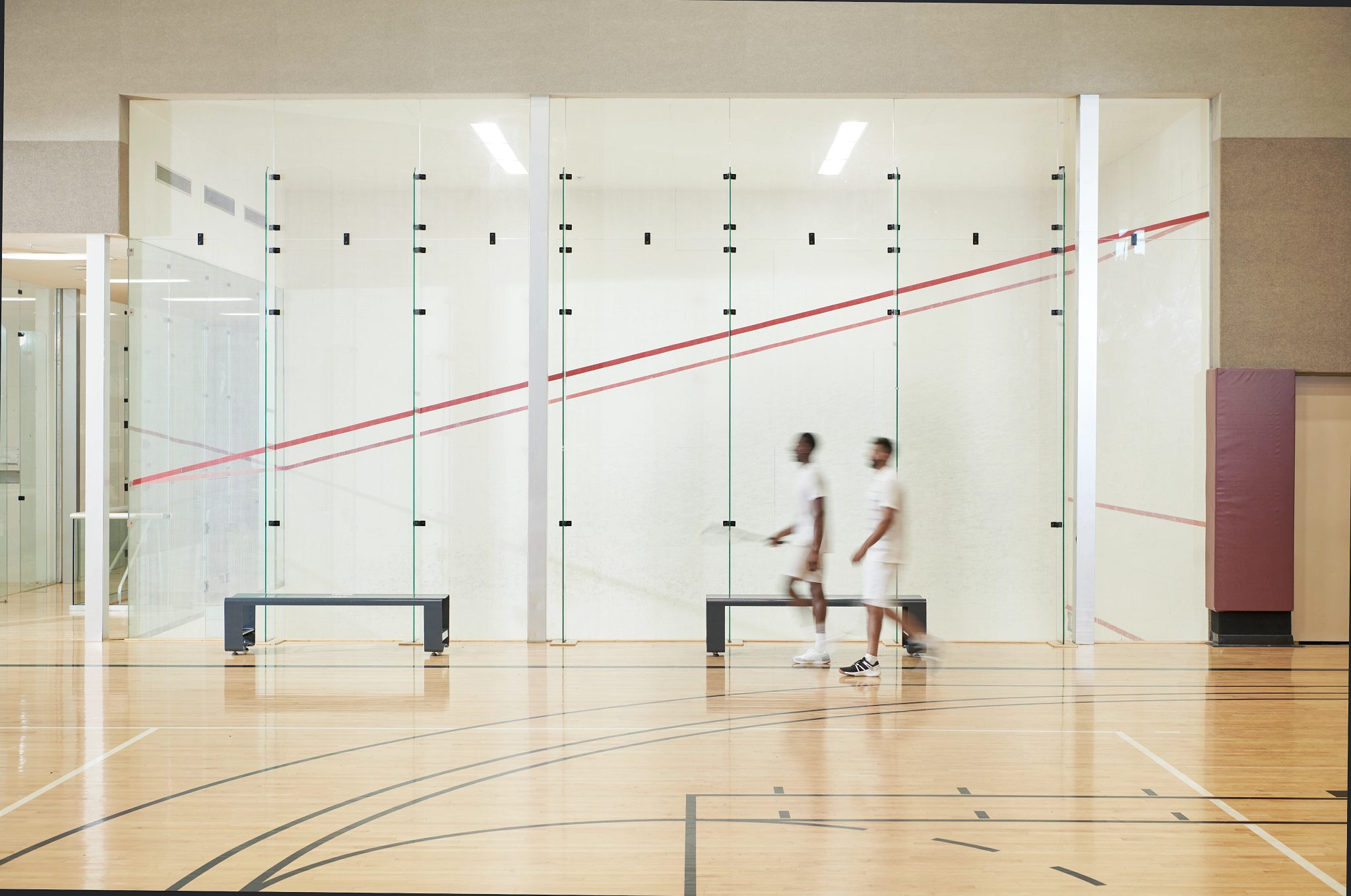 Two men walking by an open squash court at the Life Time South Austin club location