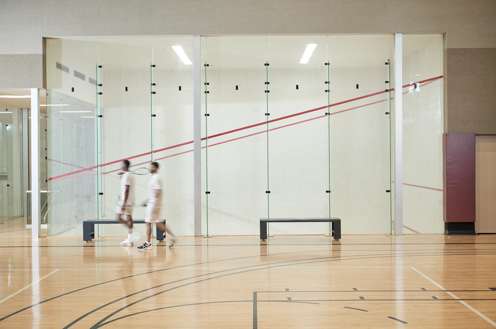 Two men walking by an open squash court at the Life Time South Austin club location