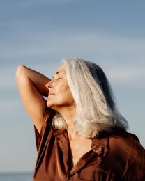 Active mature beautiful woman enjoying the beach in the morning wearing brown dress in front of the sea
