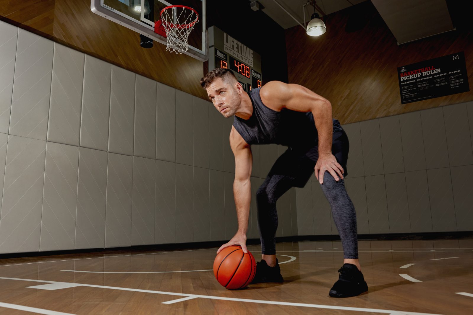An adult man bent over holding a basketball on a wooden basketball court