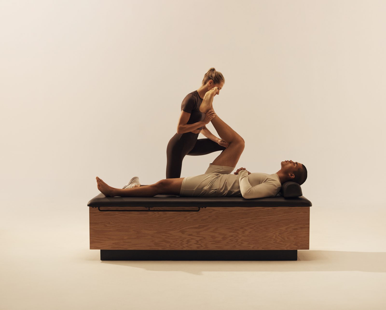 Trainer stretching a client's leg towards his chest while he lays on his back on a stretch table