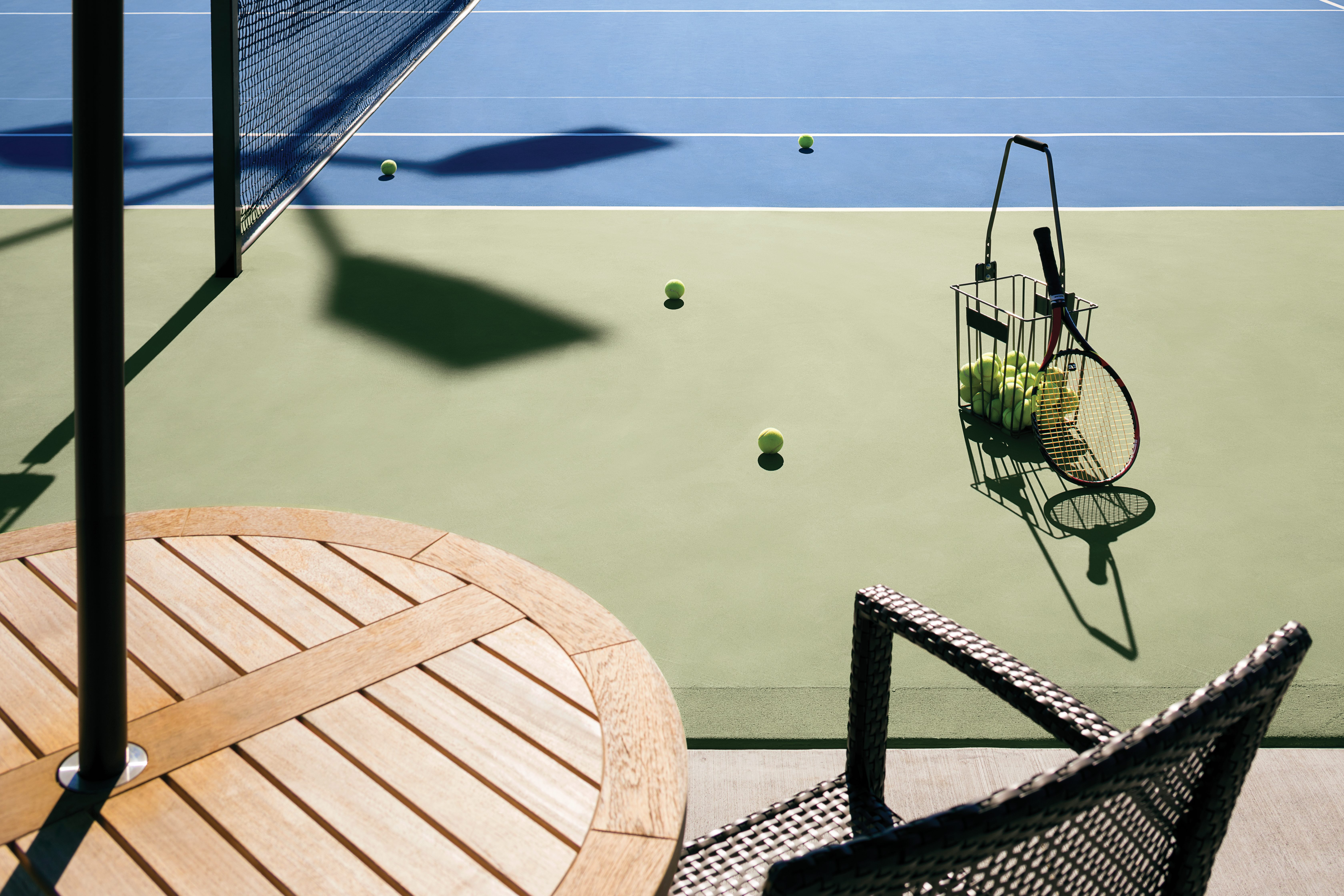 A basket of tennis balls and racquet on a tennis court