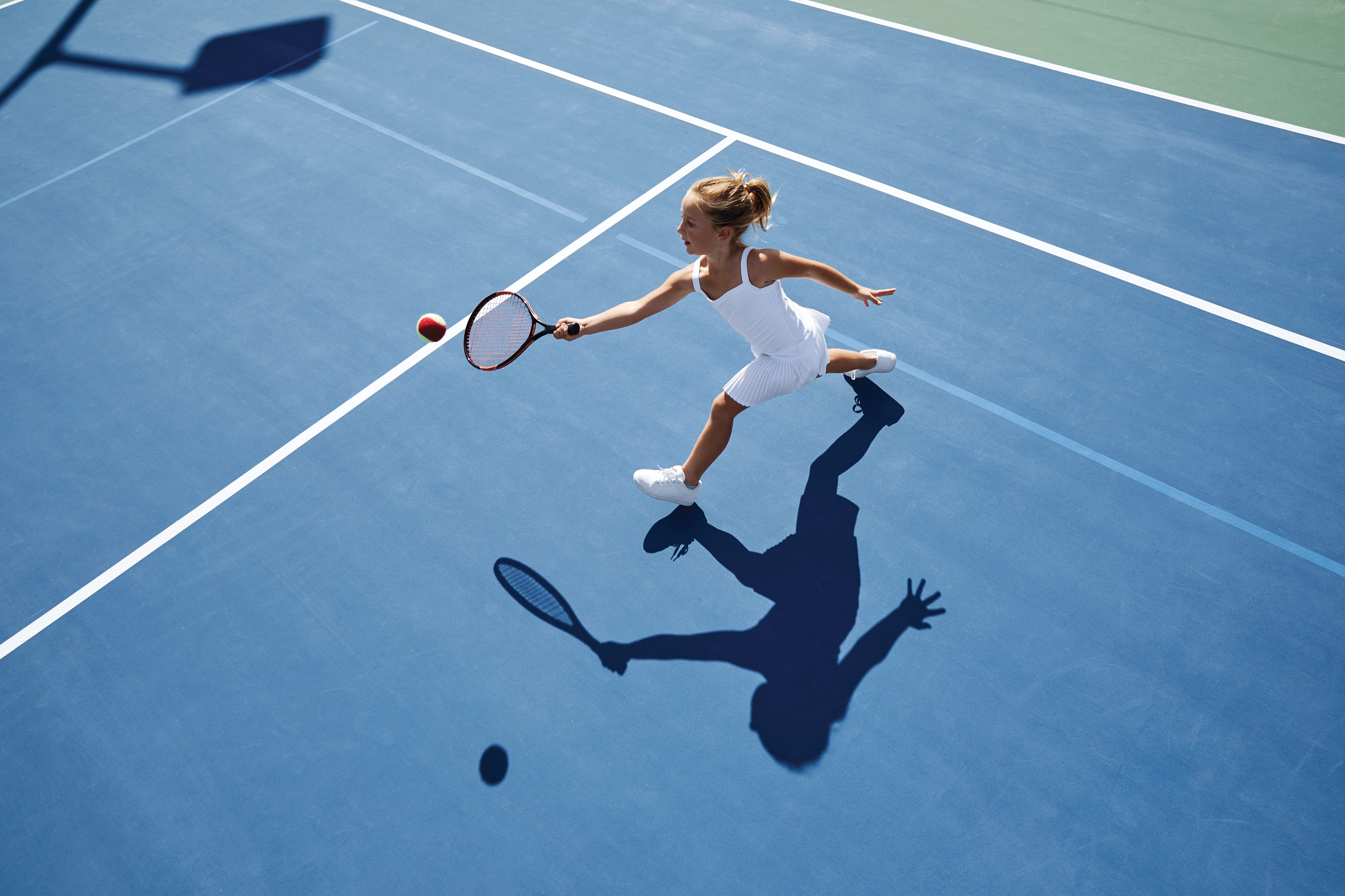 Aerial view of a young girl playing tennis on an outdoor tennis court