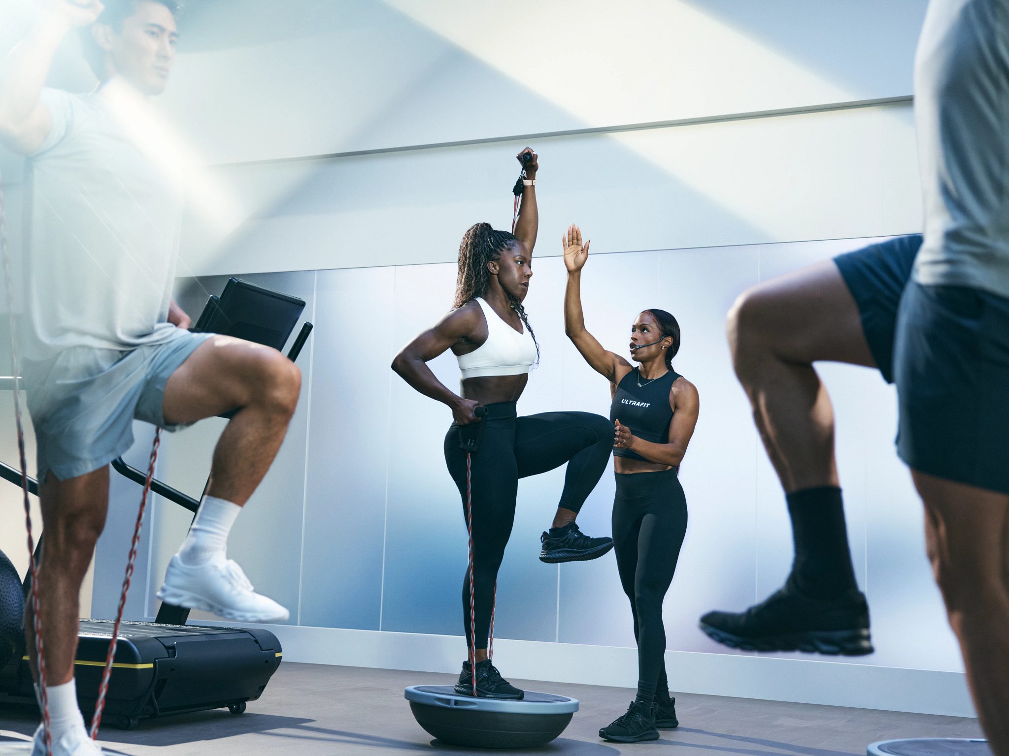Person balancing on a bosu ball on one foot being guided by an UltraFit instructor