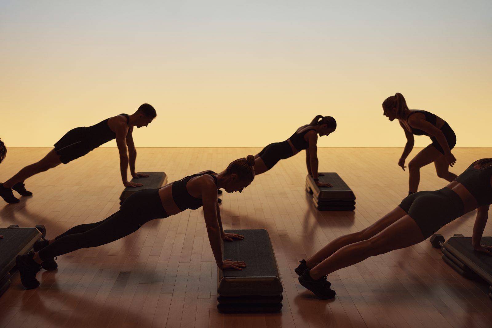 Xtreme cardio class members in elevated plank being encouraged by a Life Time instructor