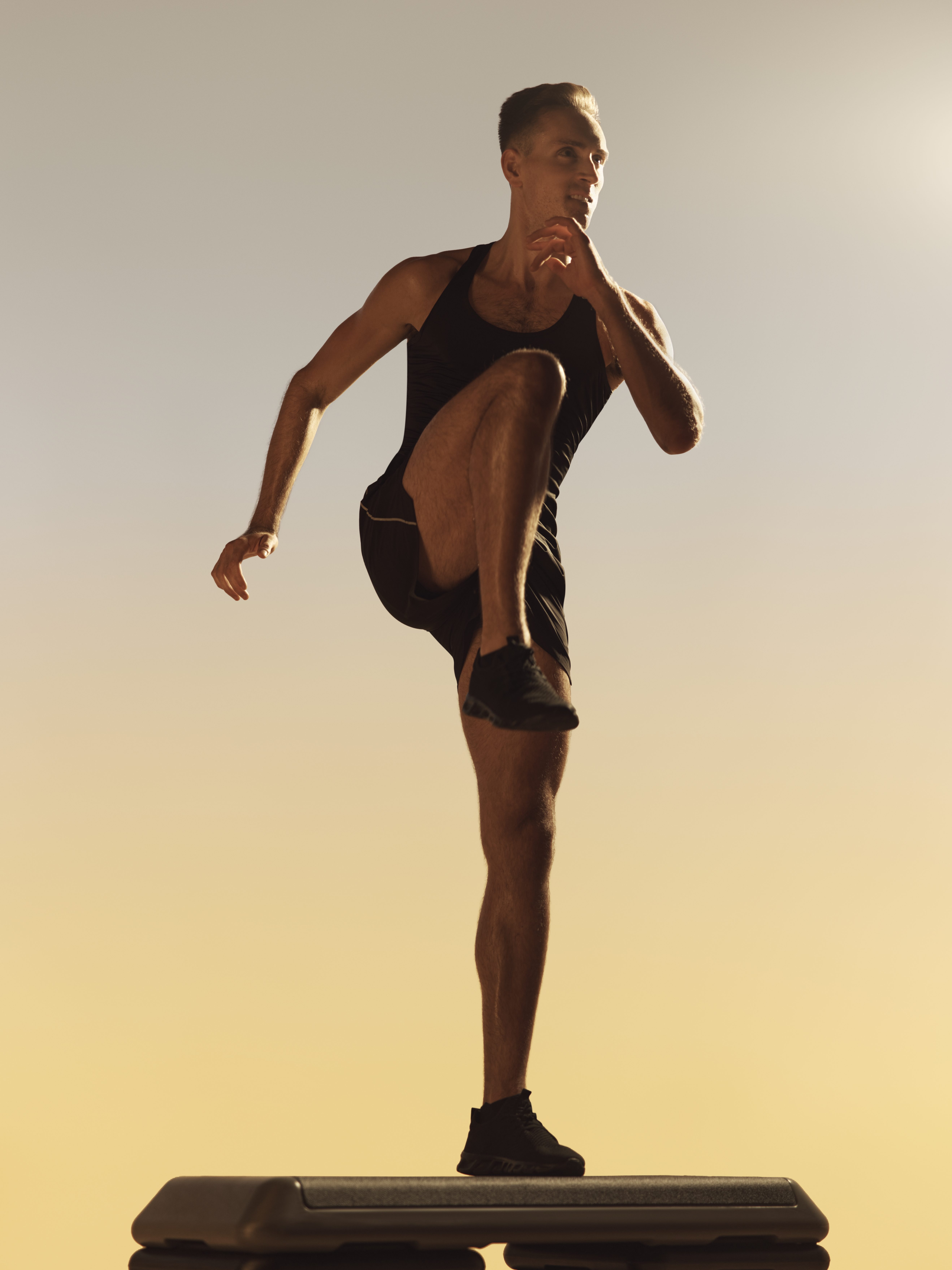 Xtreme cardio class member in a high knee lift on top of a step bench at Life Time