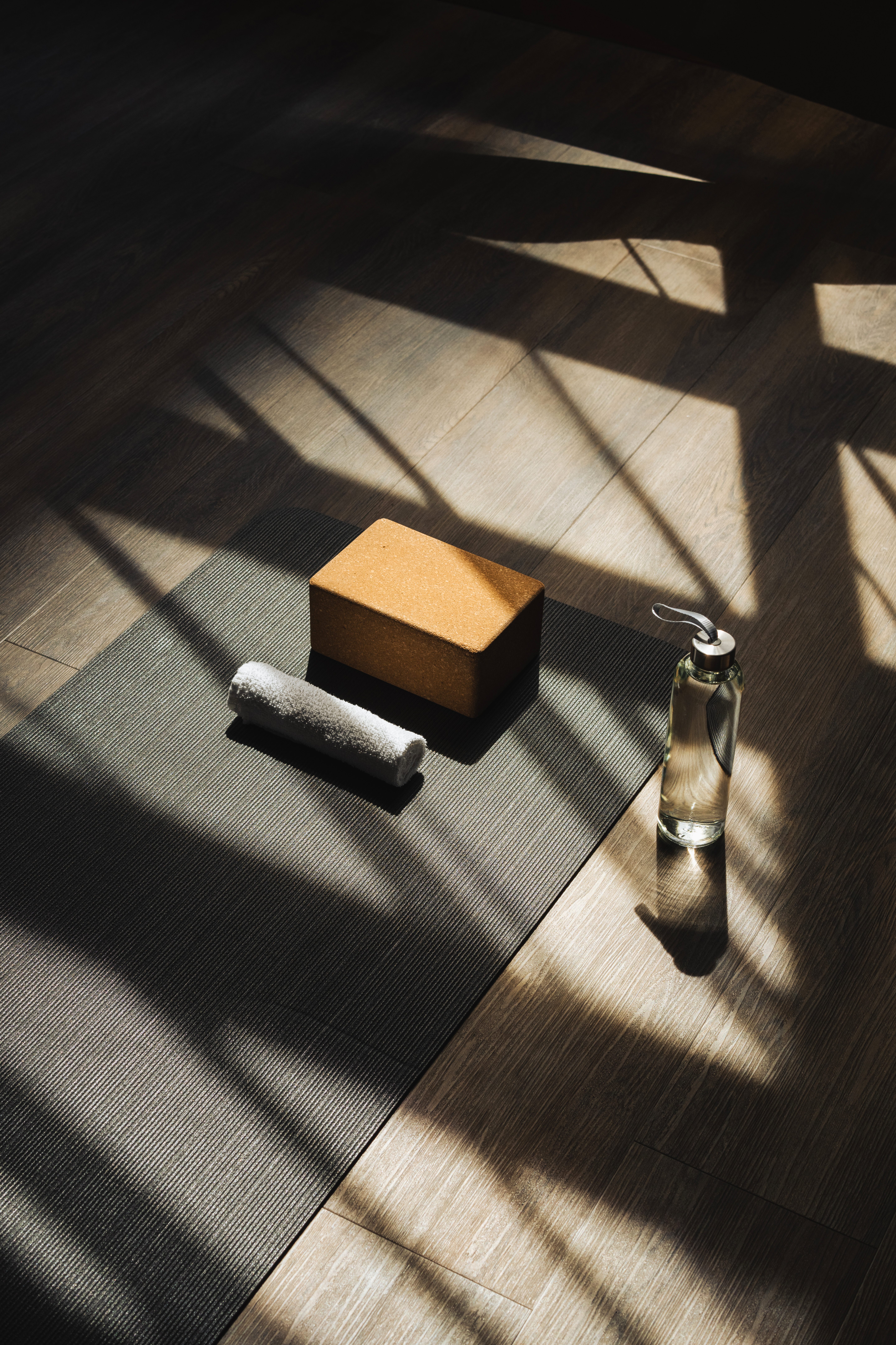 A waterbottle, yoga block, and towel sit by a yoga mat