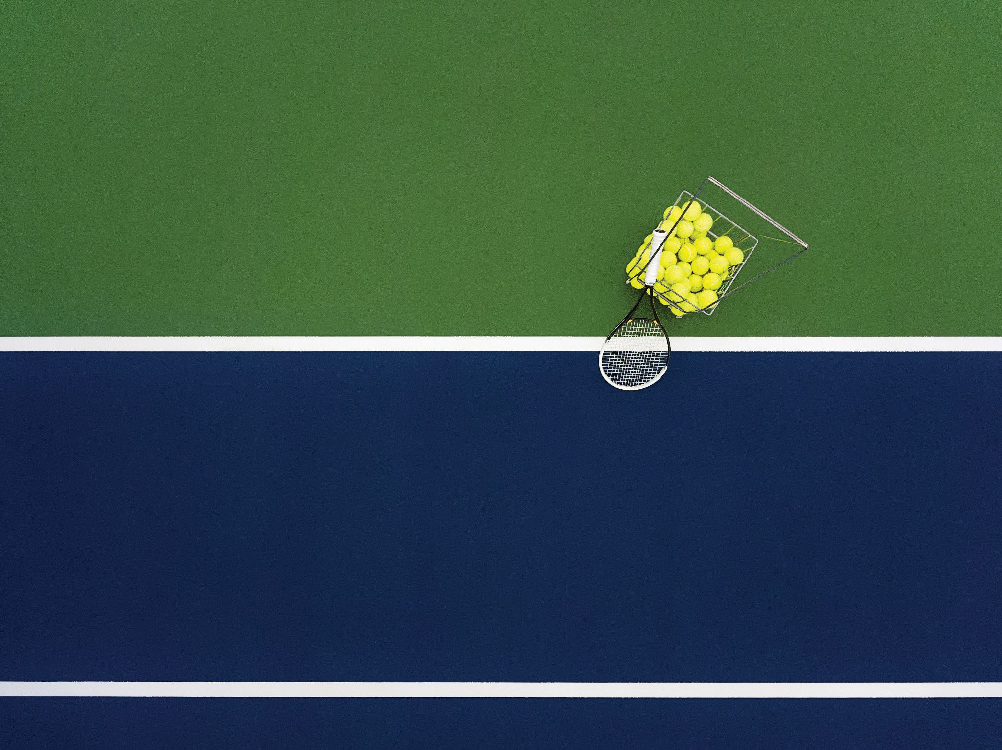 A basket of tennis balls and racquet on a tennis court