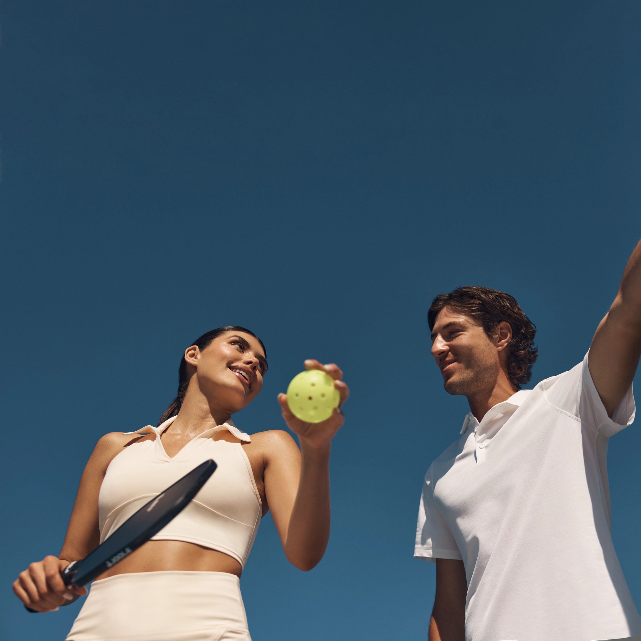 Two pickleball players looking at each other while holding a ball and paddle