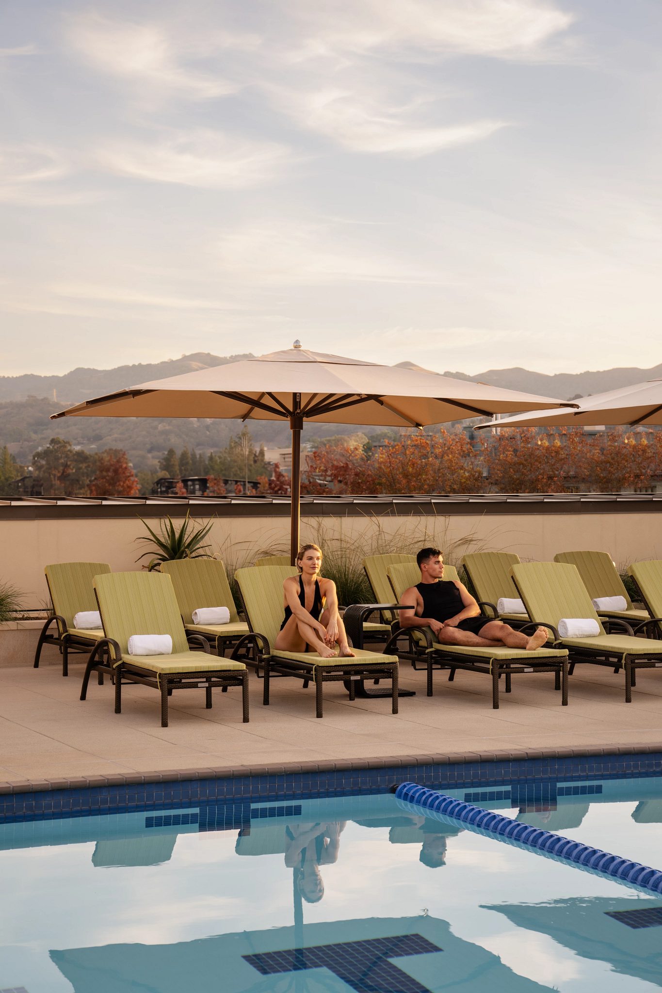 a man and woman sit on lounge chairs by an outdoor pool