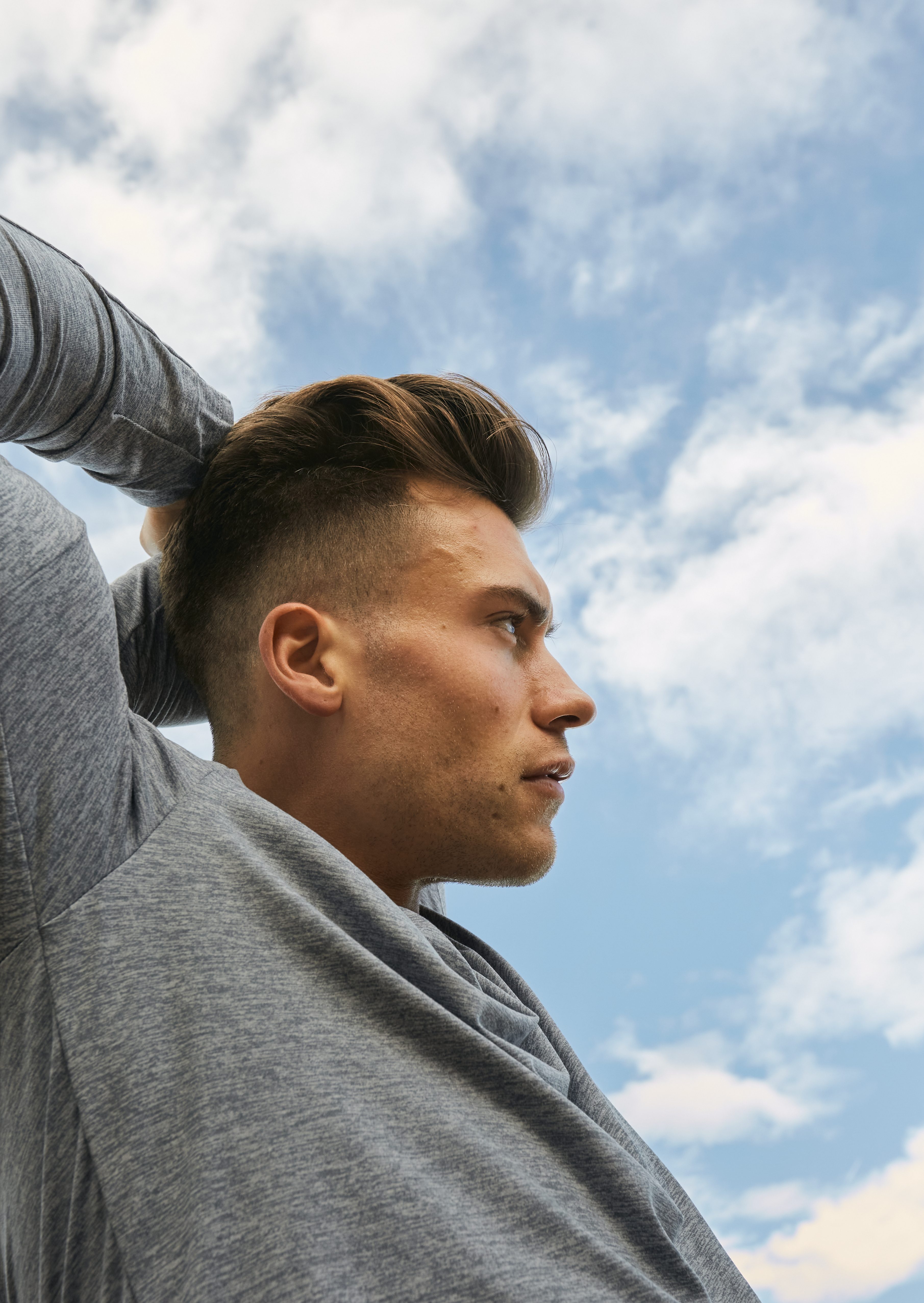 A young man exercising outside and stretching his arm over his head