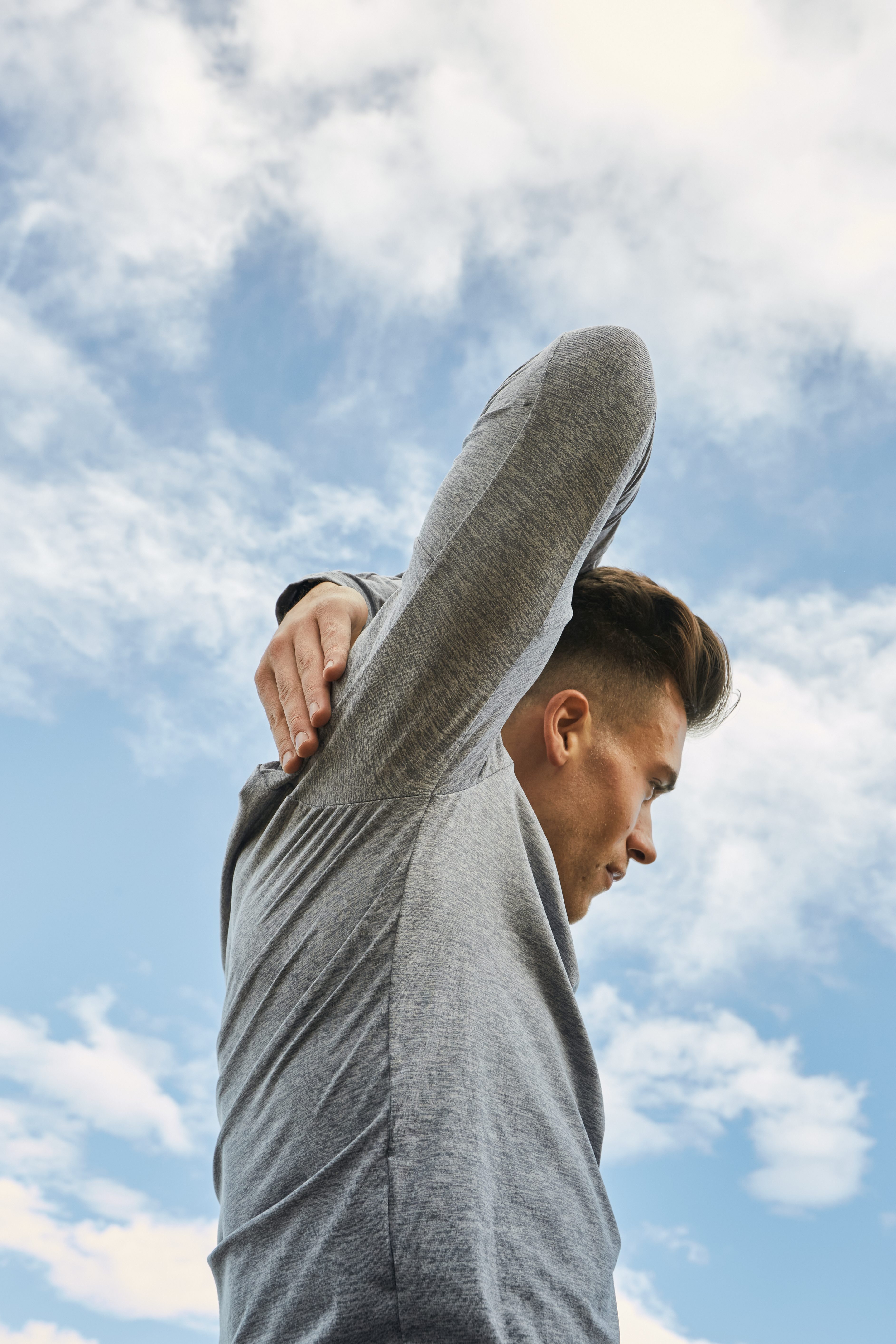 A young man exercising outside and stretching his arm over his head