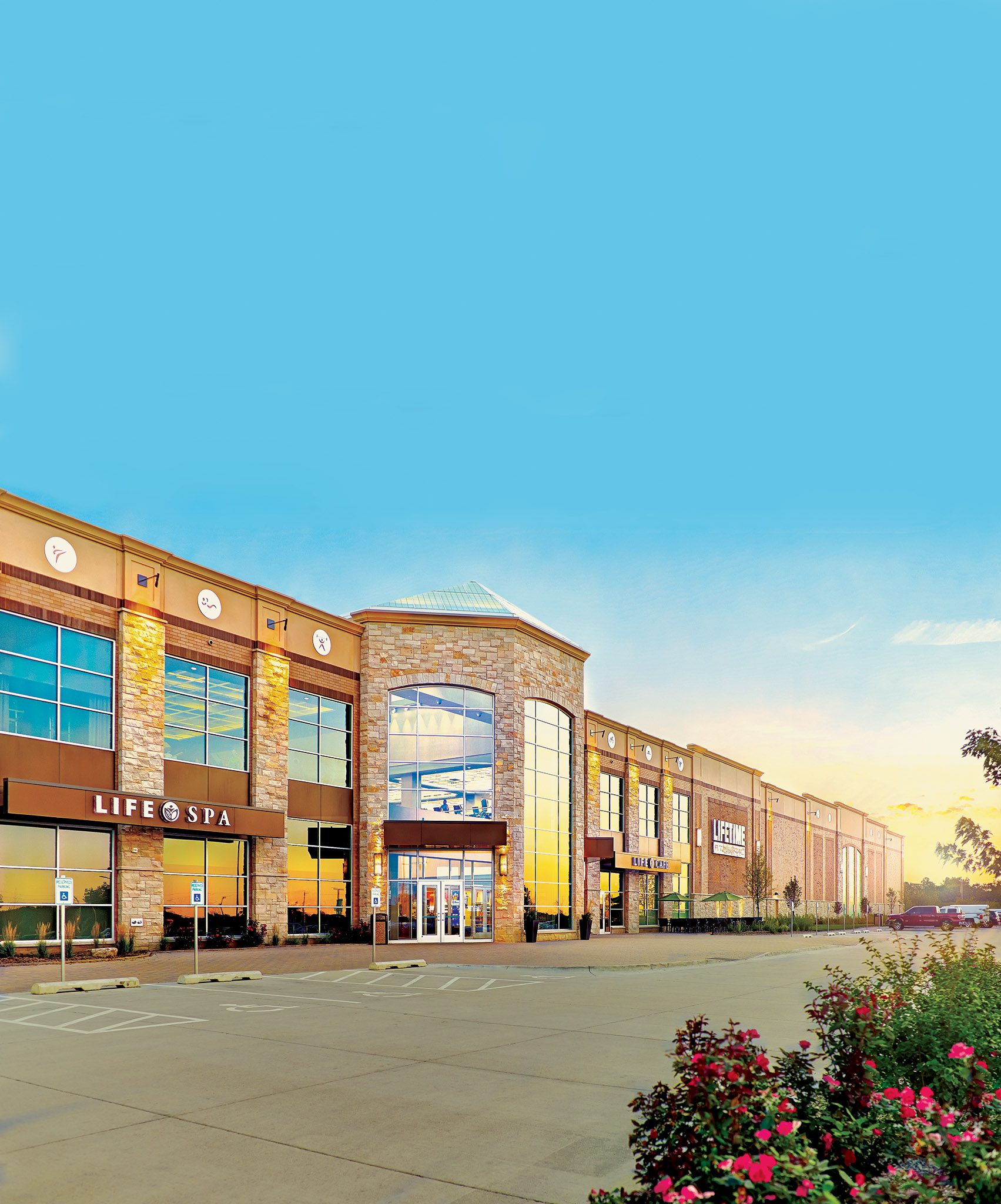 The exterior of a Life Time location on a sunny day with pink floral foliage